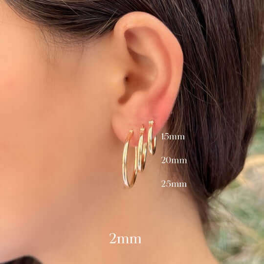 Woman wearing gold hoop earrings of varying sizes showcasing 15mm, 20mm, 25mm, and 2mm diameters from our jewelry collection.