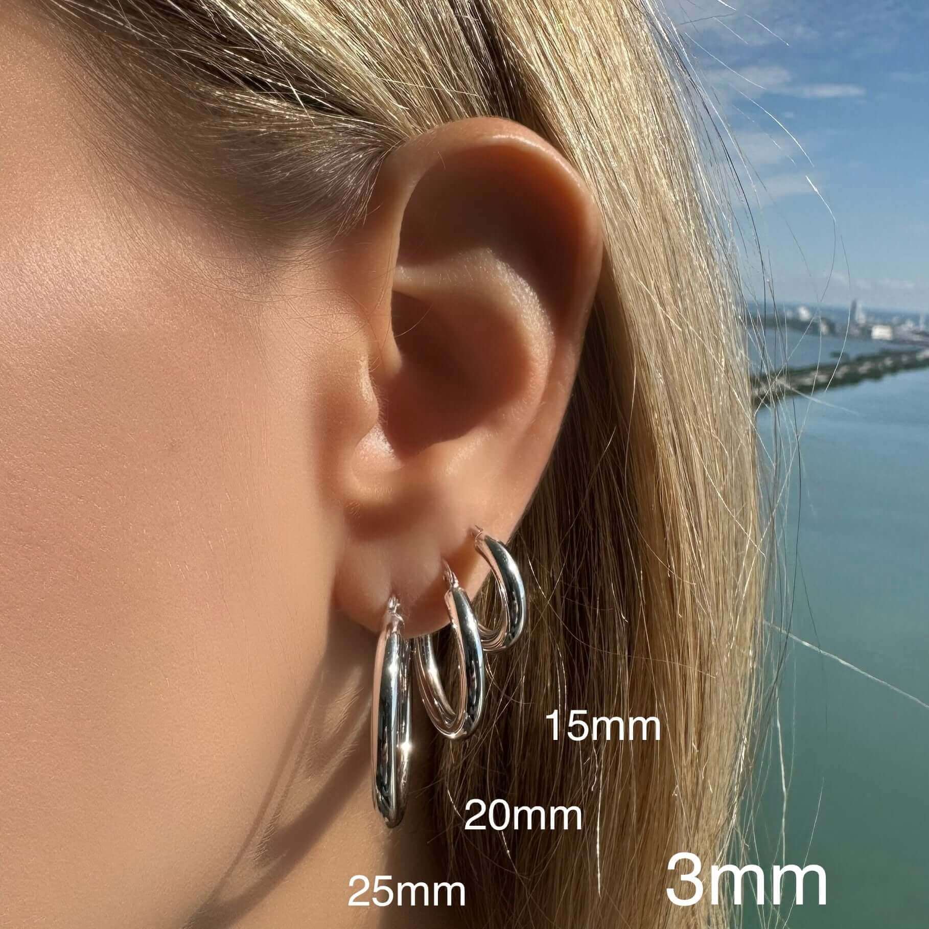Woman wearing multiple silver hoop earrings in various sizes from our jewelry collection against a scenic outdoor backdrop