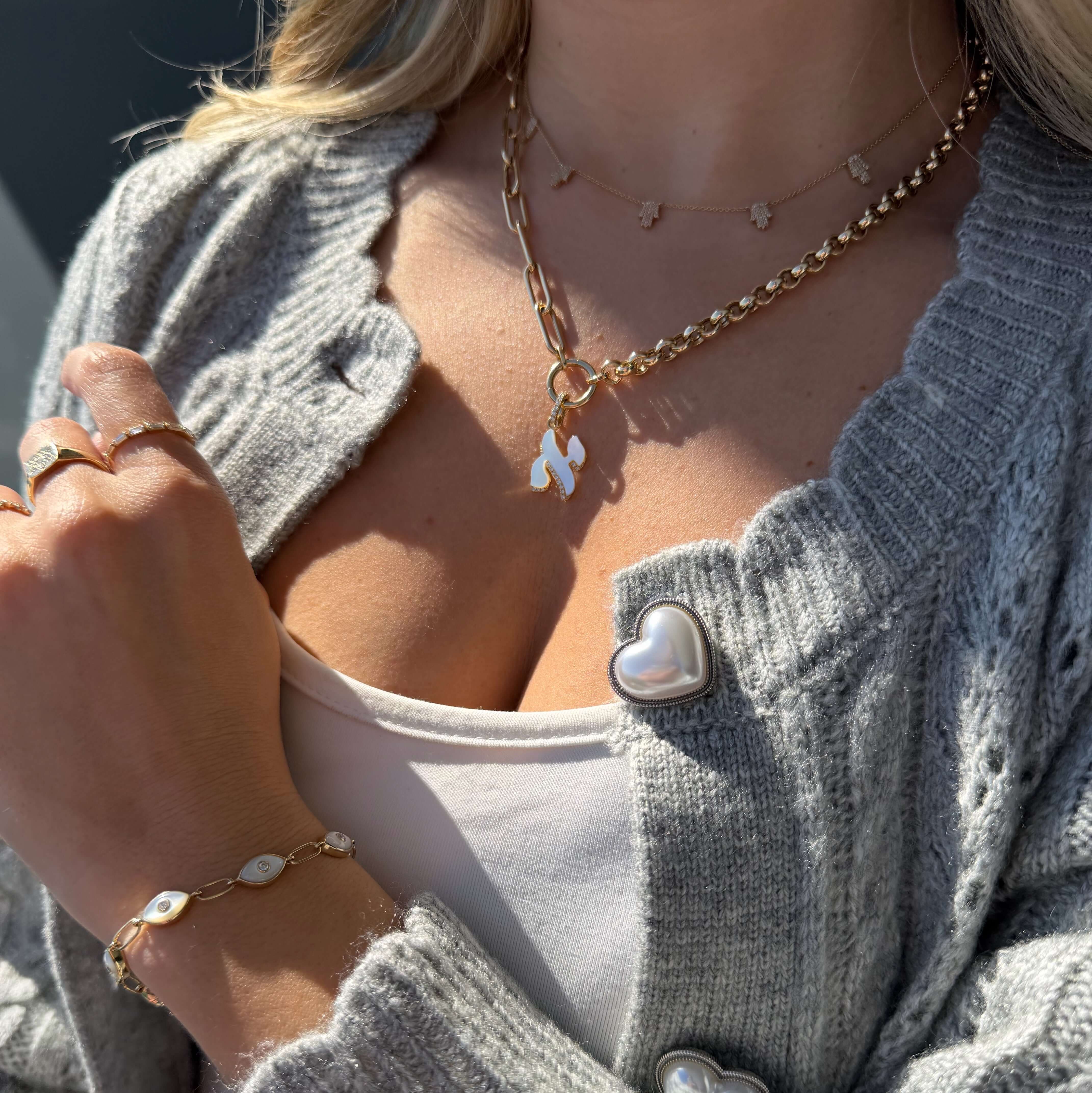 Diamond Accented Hebrew Gemstone Initial Pendant © worn with a gray cardigan, featuring gold jewelry and a pearl bracelet.
