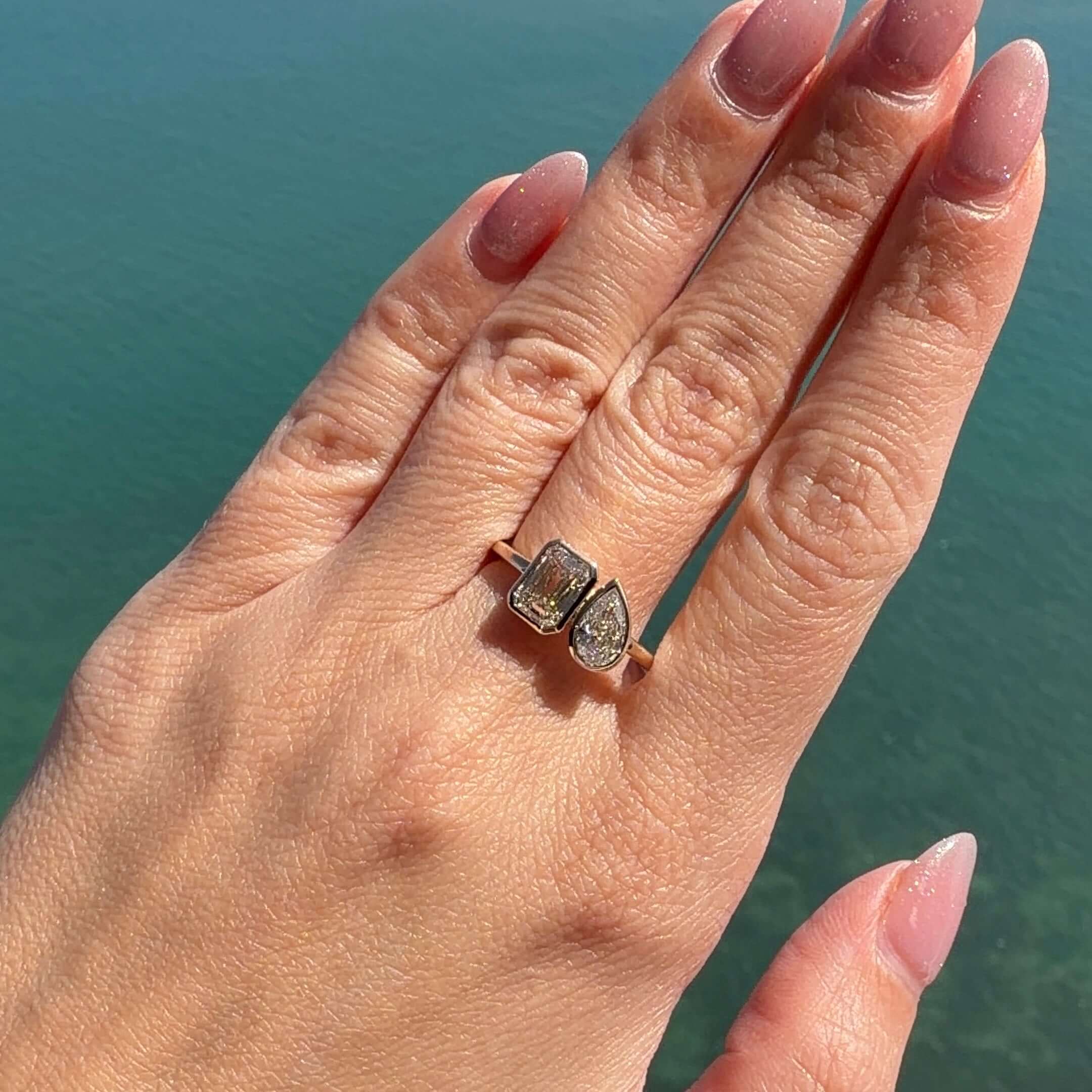 Lab Diamond Toi et Moi Bezel Ring featured on hand against a serene blue background.