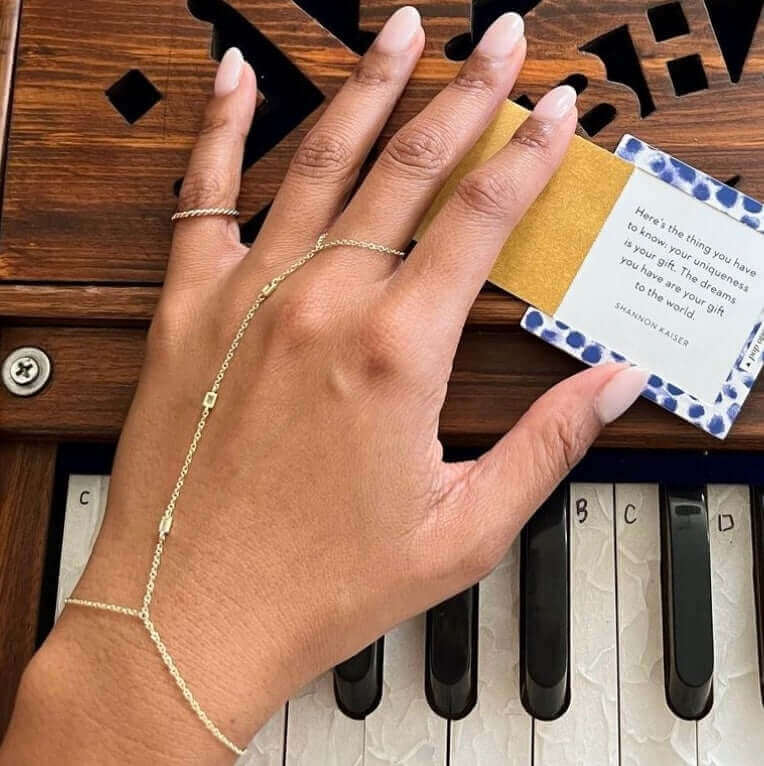 Elegant hand jewelry from our collection displayed on a hand over a piano, showcasing a stunning chain bracelet and rings.