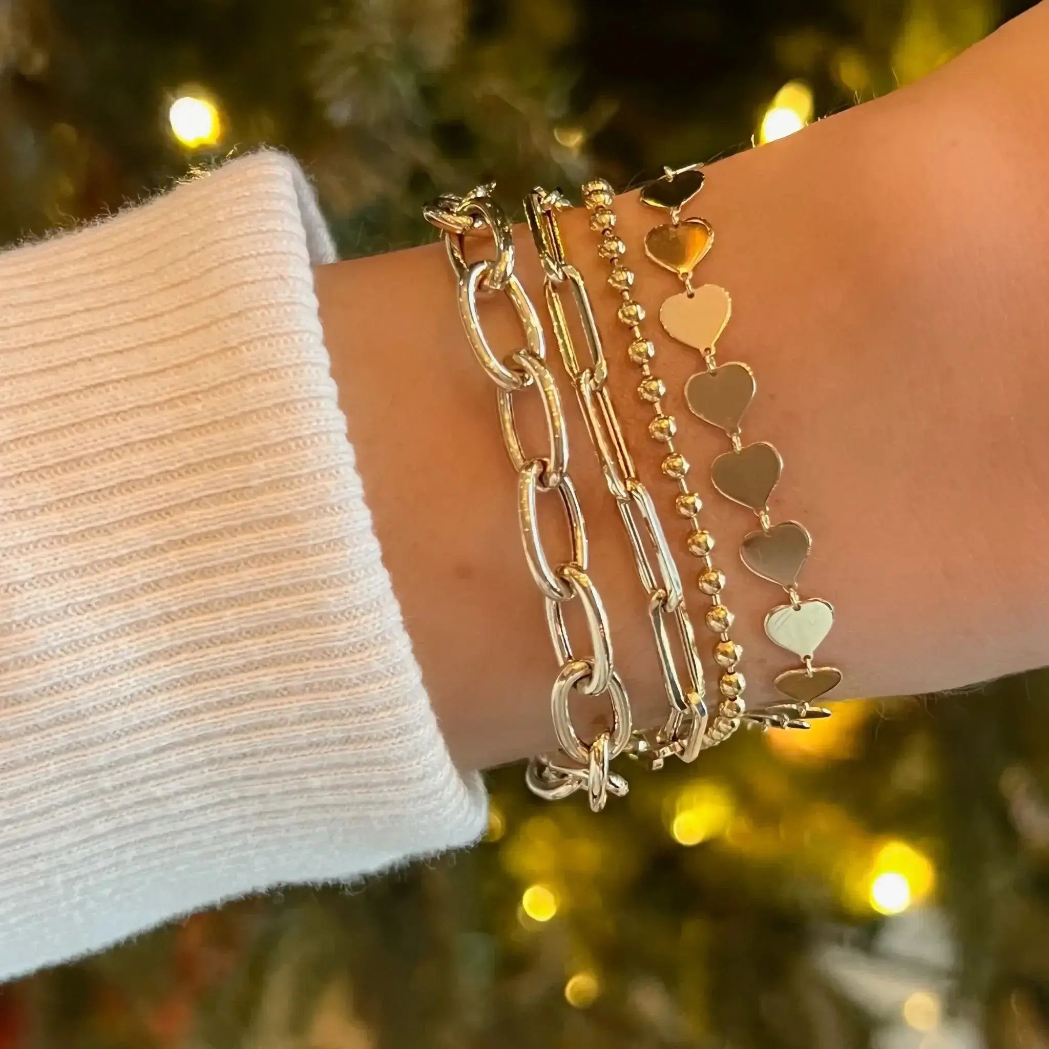 Elegant wrist adorned with layered gold bracelets from our jewelry collection, featuring heart and chain designs.