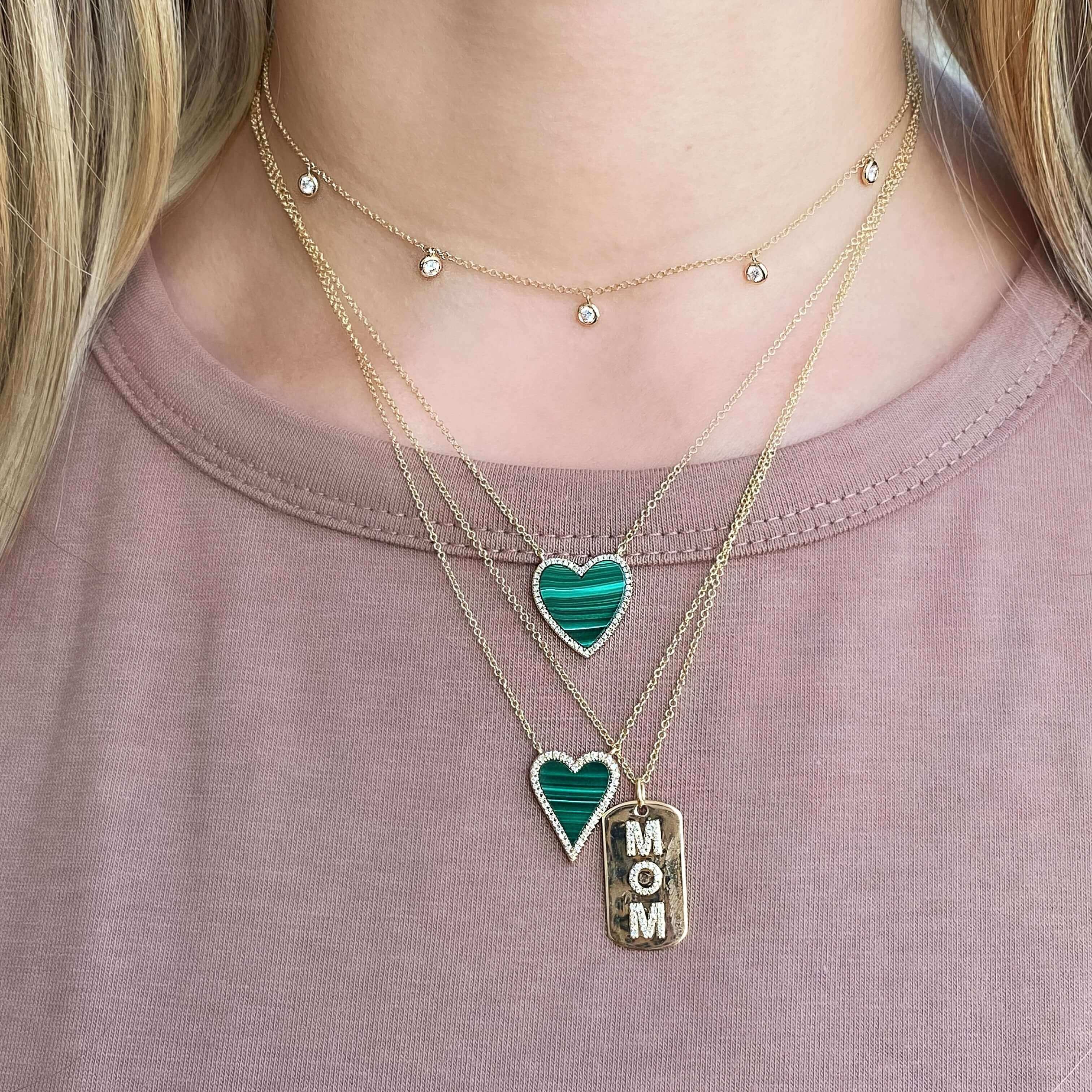 Woman wearing layered necklaces with green heart pendants and a 'MOM' charm, part of our elegant jewelry collection.