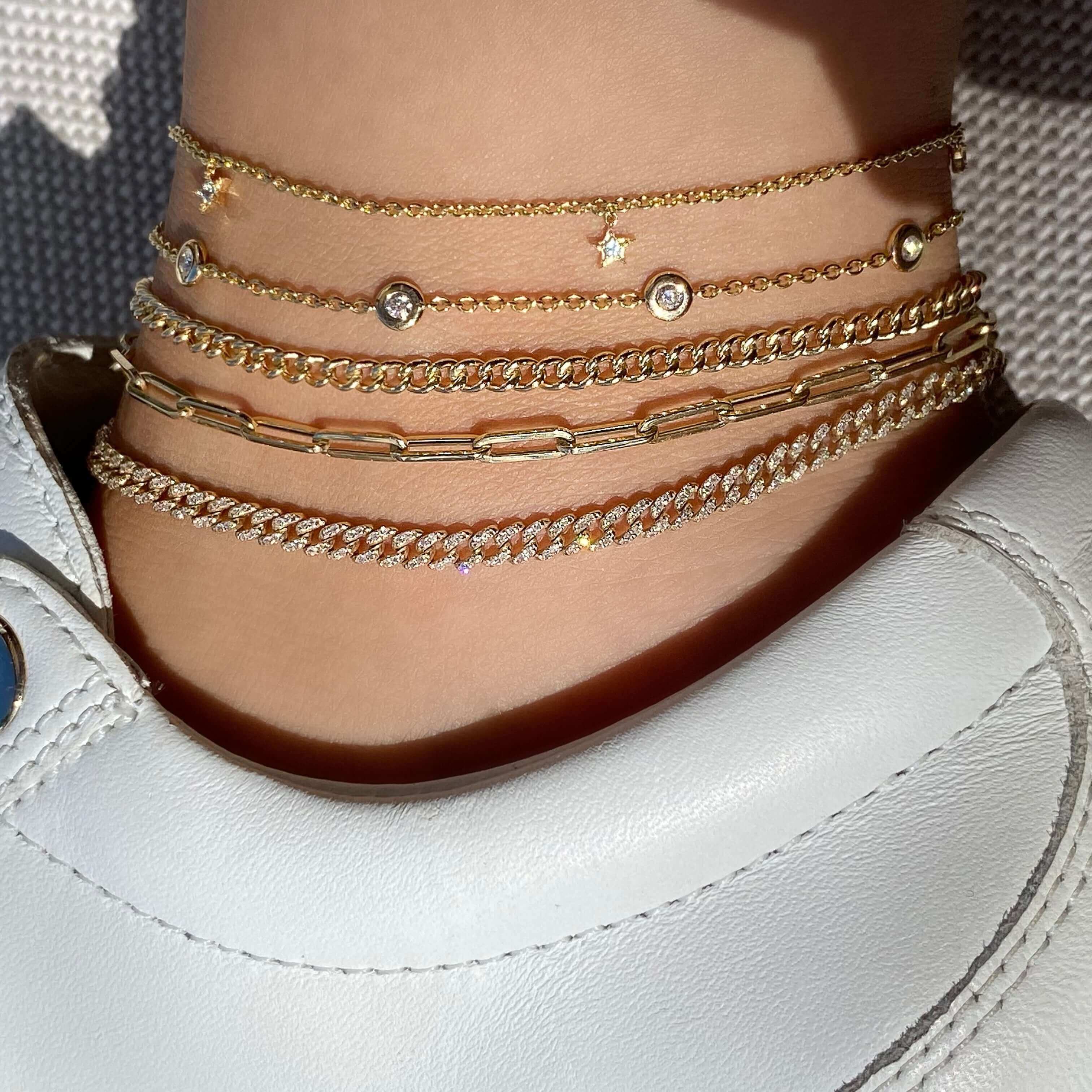 Stylish gold anklets from our jewelry brand displayed on a person’s ankle in white shoe.