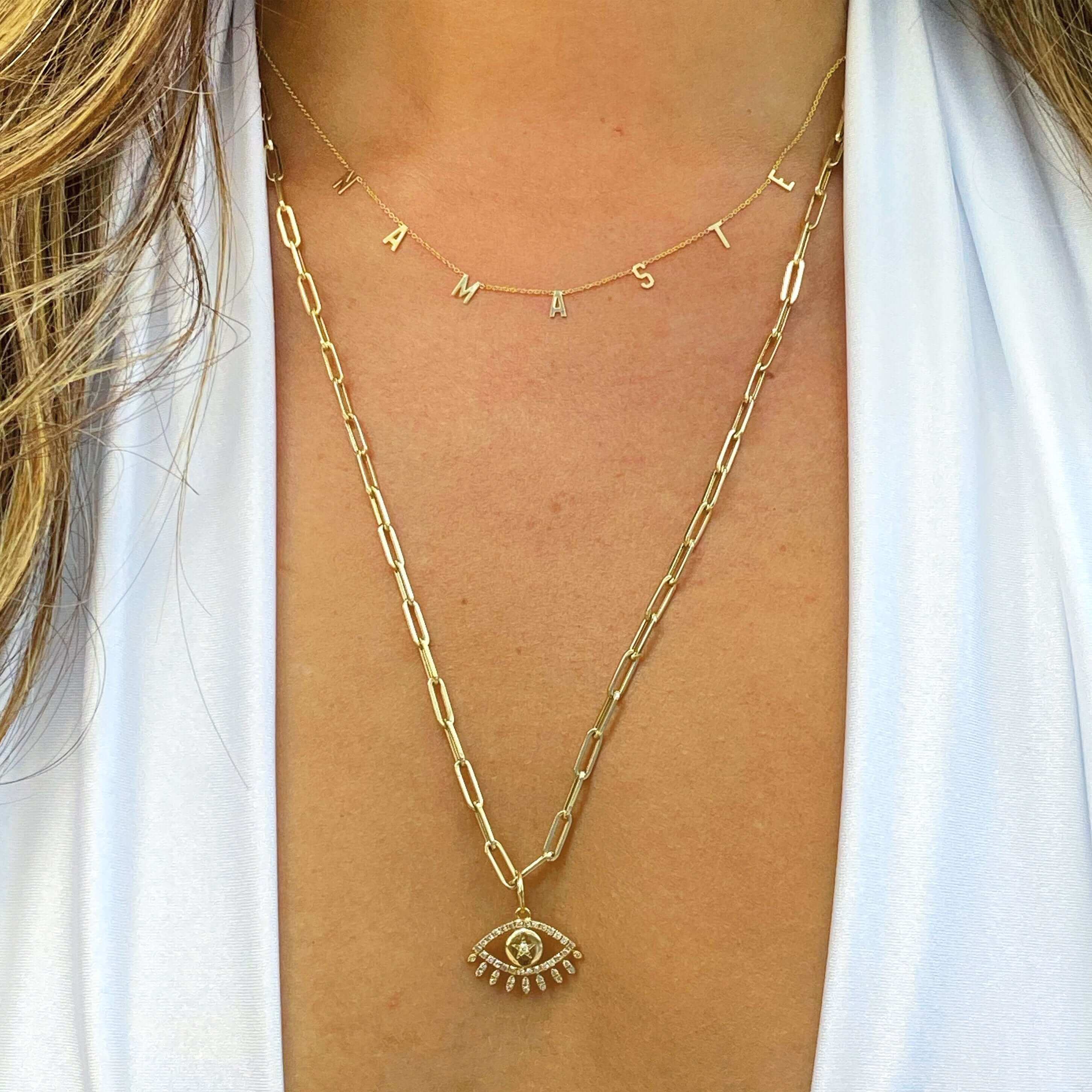 Woman wearing layered gold necklaces with namaste and evil eye pendants from our jewelry collection.