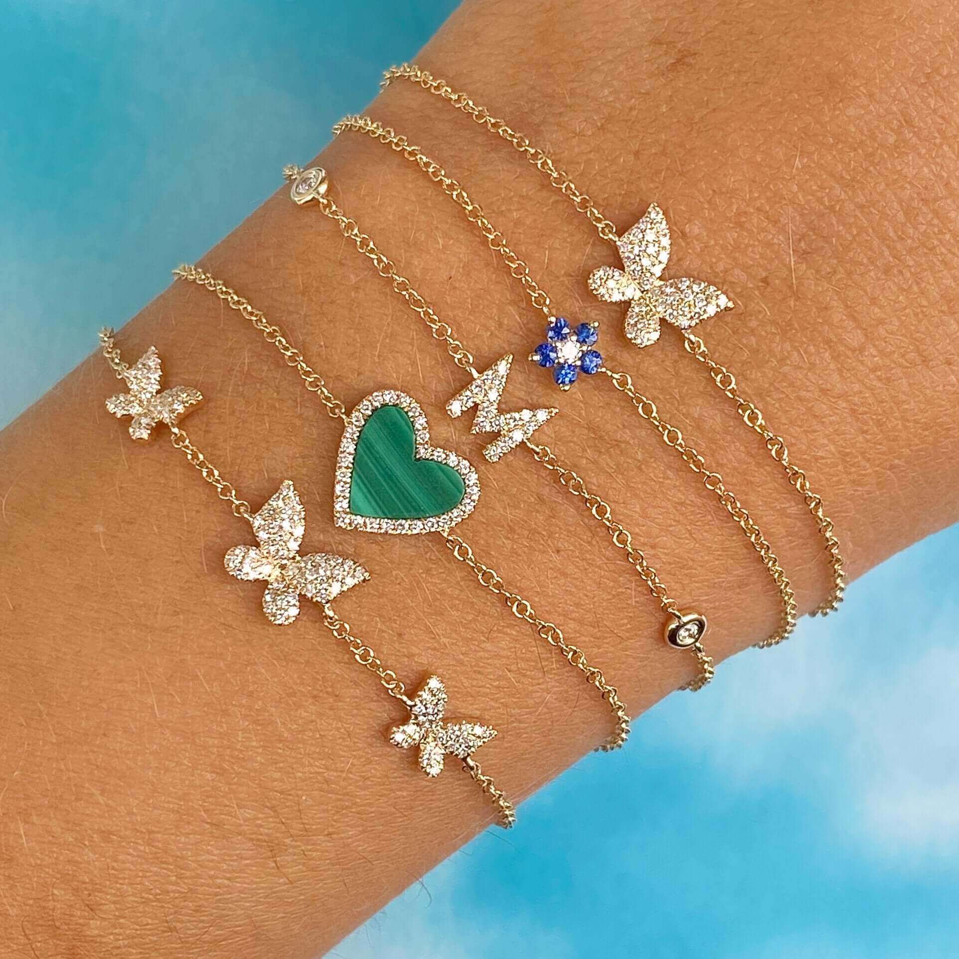 Elegant gold bracelets with butterfly and heart charms, accented with blue and green stones from our jewelry brand's exclusive collection