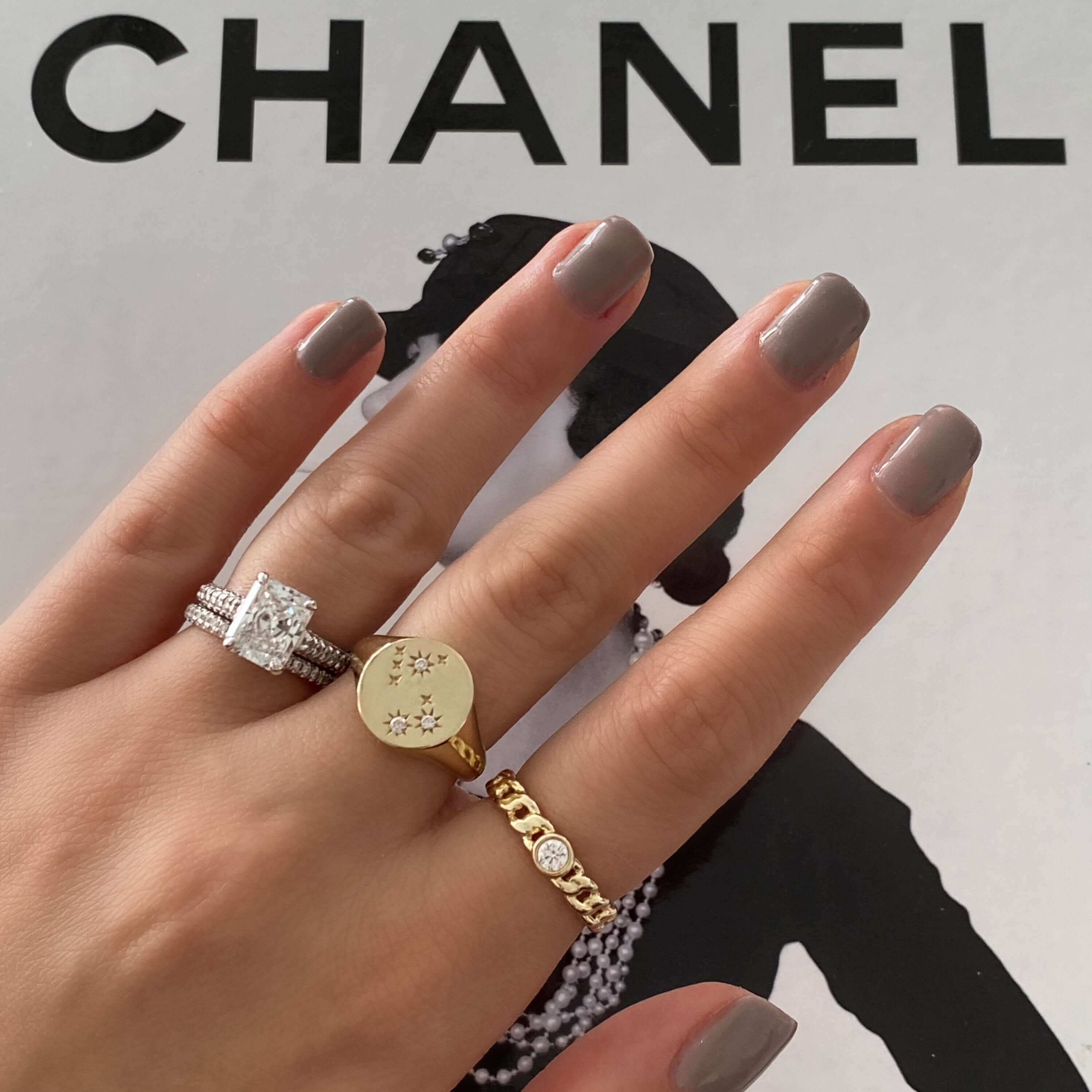 Elegant hand with a gold star-engraved ring and diamond-studded jewelry on a Chanel background by our jewelry brand.