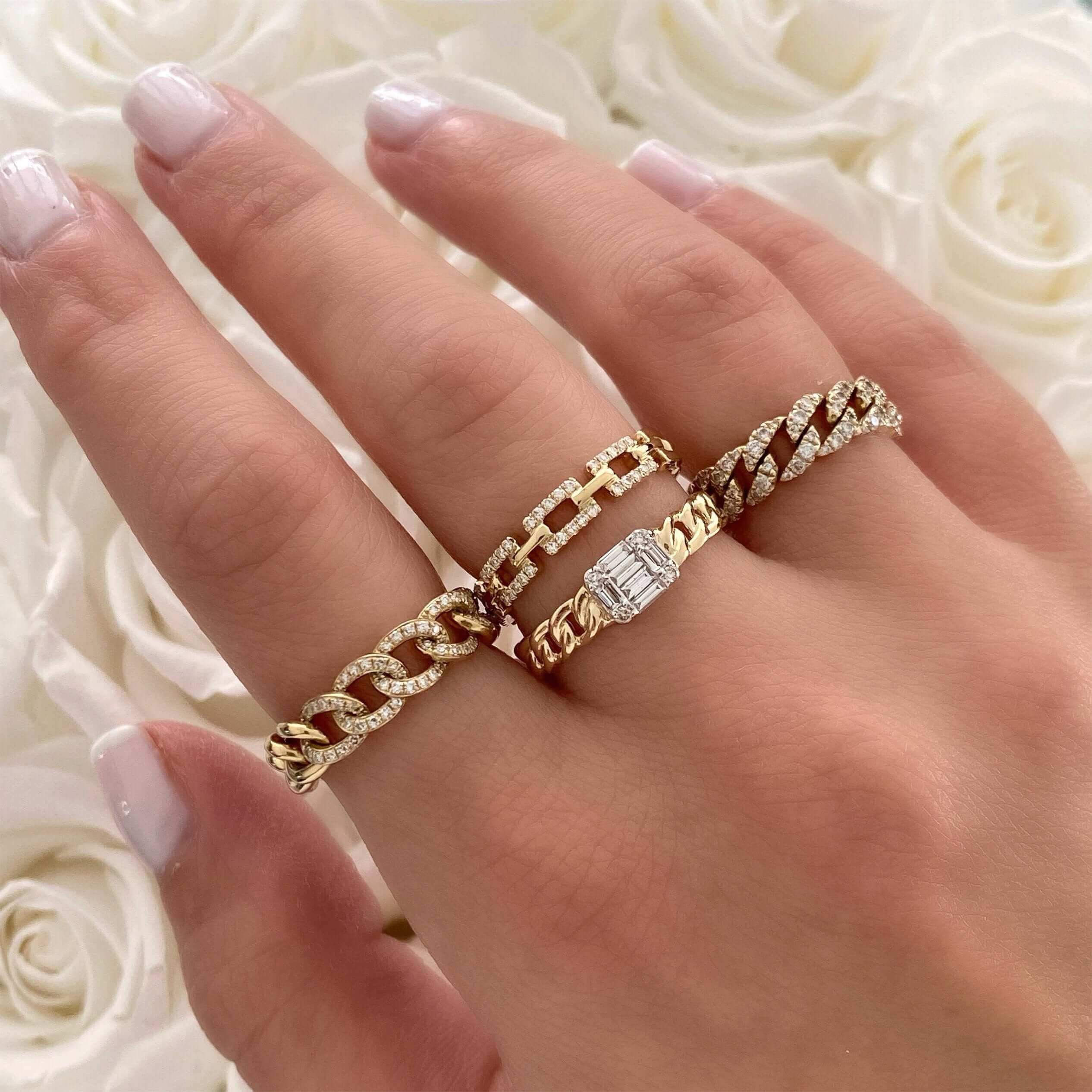 Elegant rose gold and diamond chain link rings on hand with white rose petals in the background.