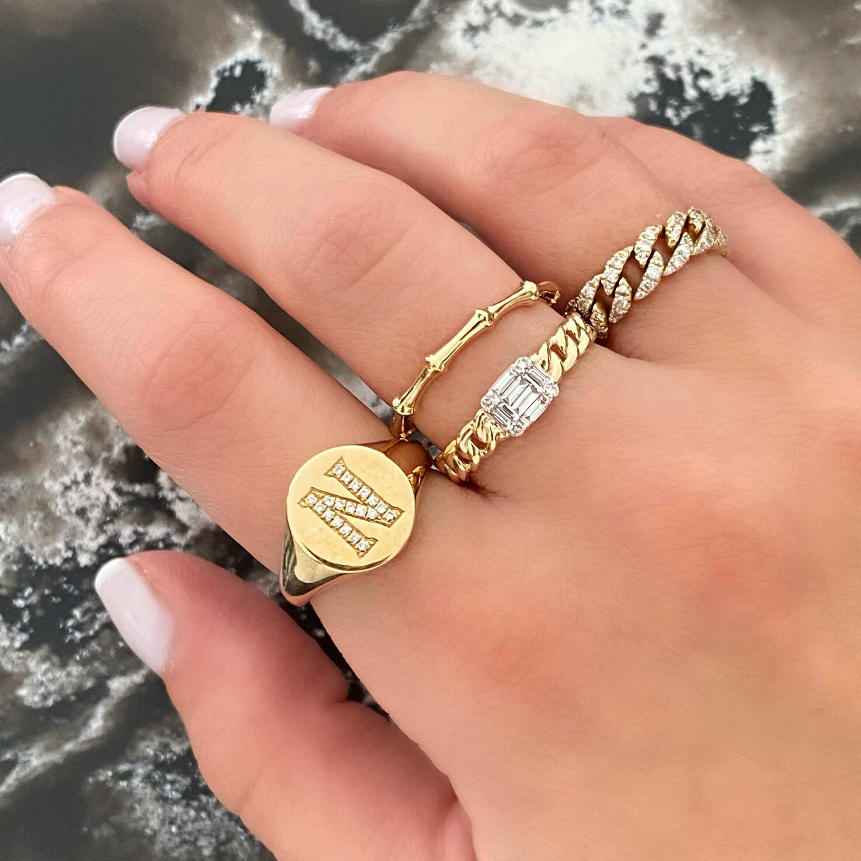 Hand adorned with elegant gold rings featuring a personalized signet and diamond accents, showcasing our luxurious jewelry collection.