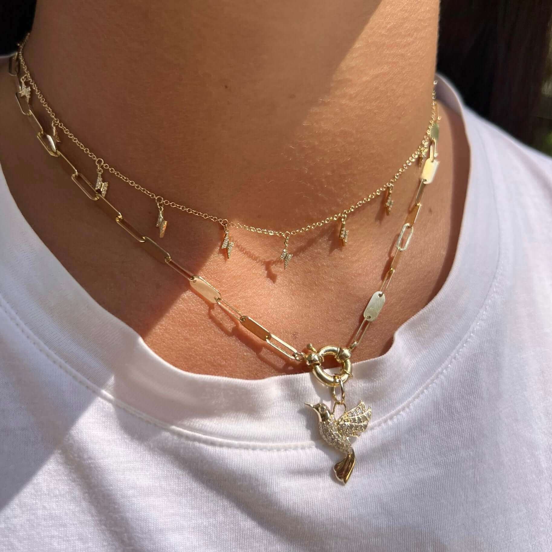 Double-layer gold necklace with delicate pendants and a bird charm from our jewelry brand, styled on a person wearing a white shirt.