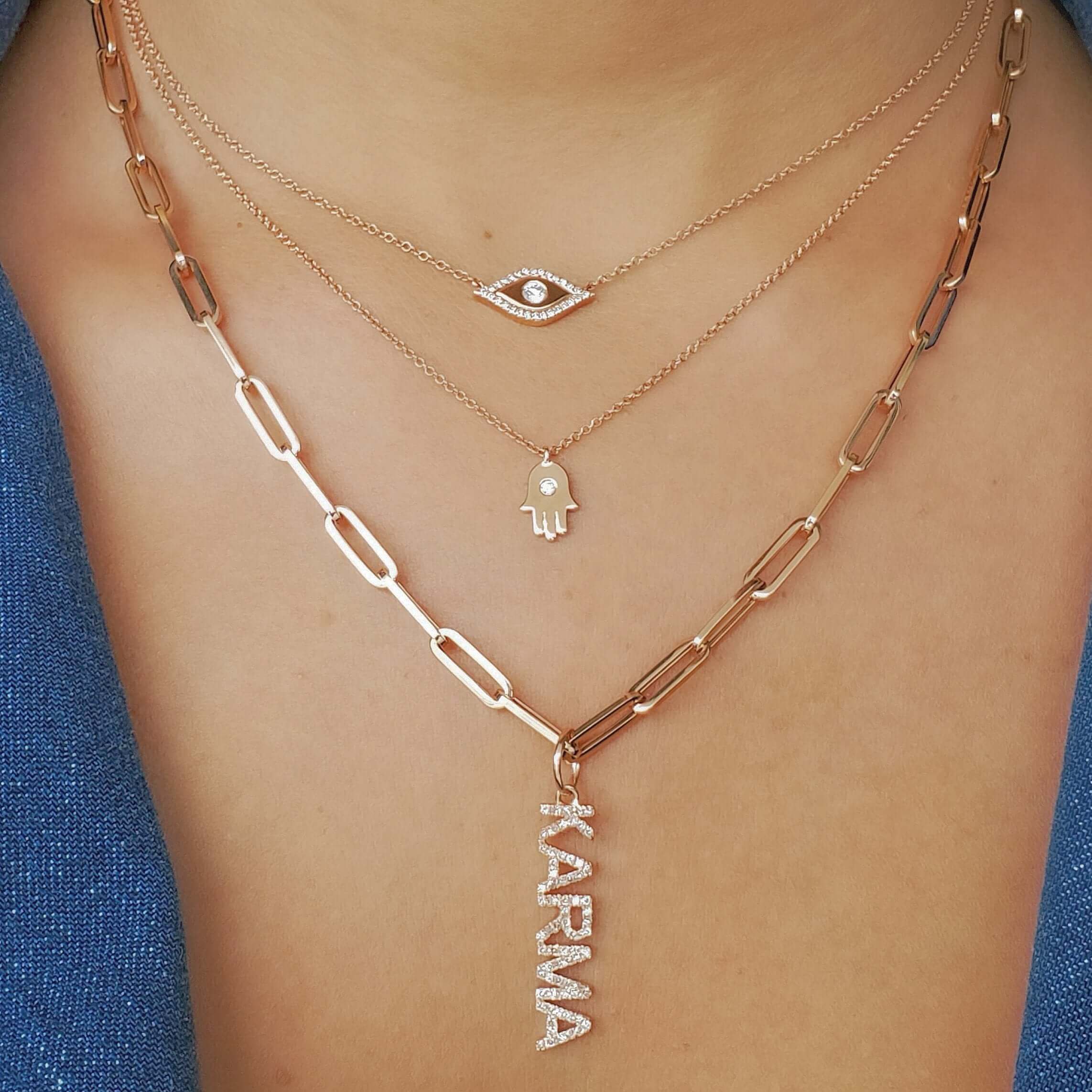 Woman wearing layered rose gold necklaces with karma pendant, evil eye, and hamsa hand charms from our jewelry brand.