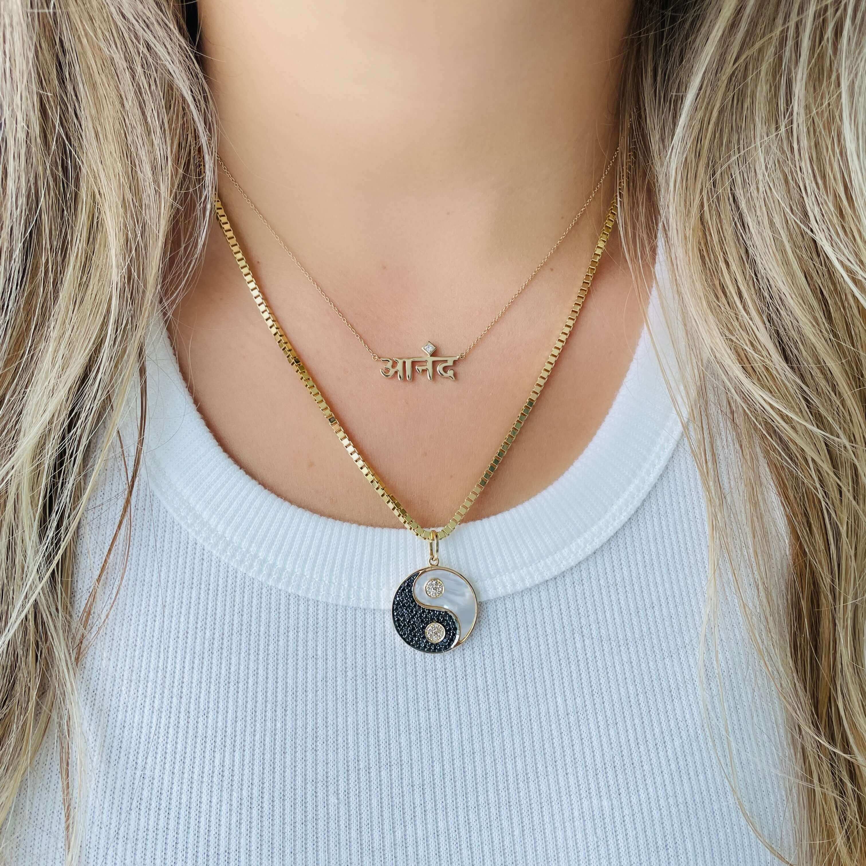 Woman wearing layered gold yin yang necklace and delicate script necklace