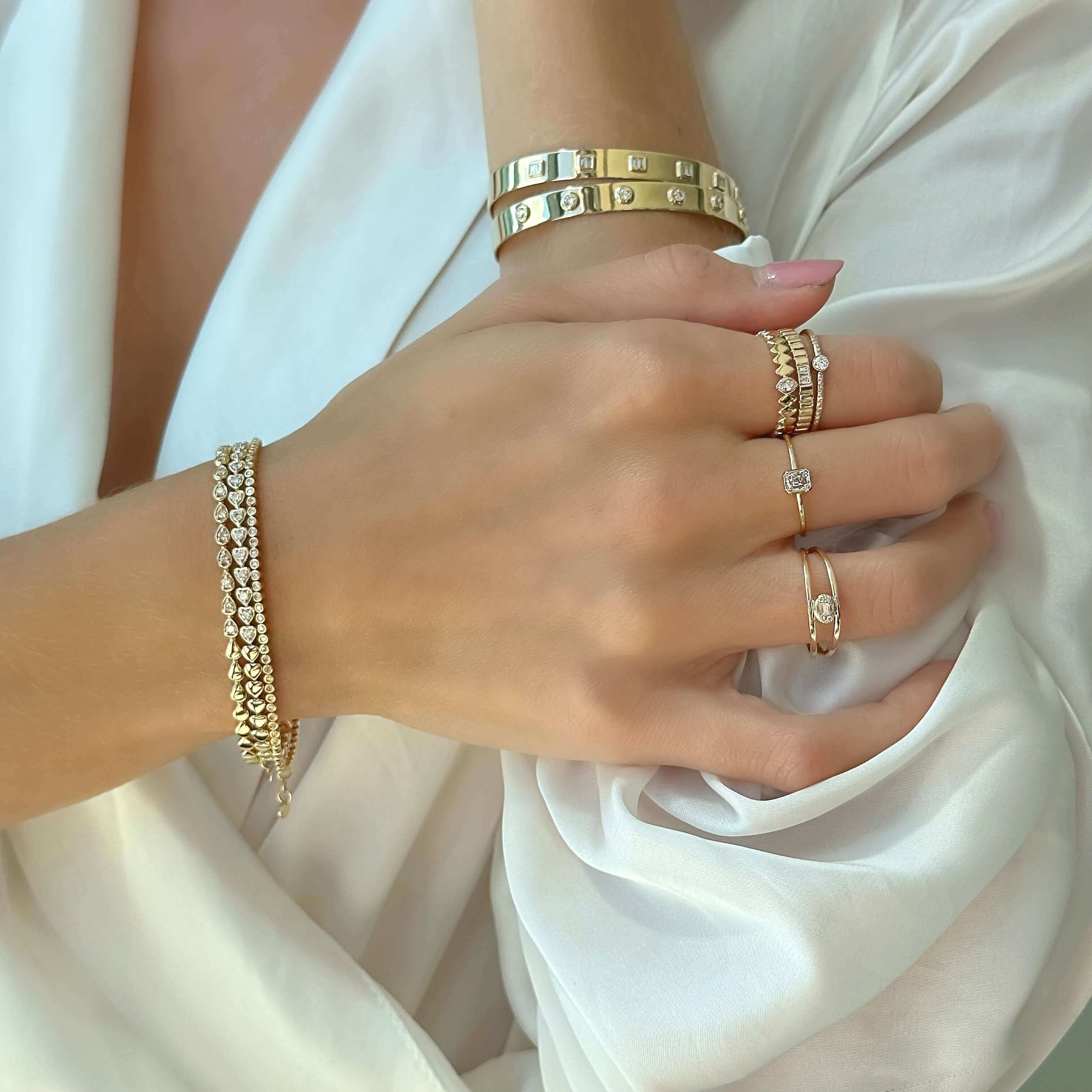 Elegant woman wearing gold bangle bracelet and diamond-studded rings gracefully showcases our luxury jewelry collection.