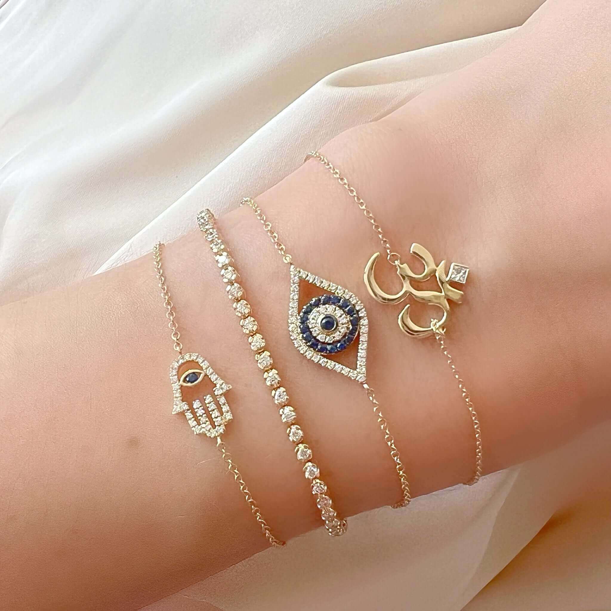Elegant gold and silver bracelets with symbolic charms on wrist, including hamsa, evil eye, crystals, and infinity design from our jewelry brand.
