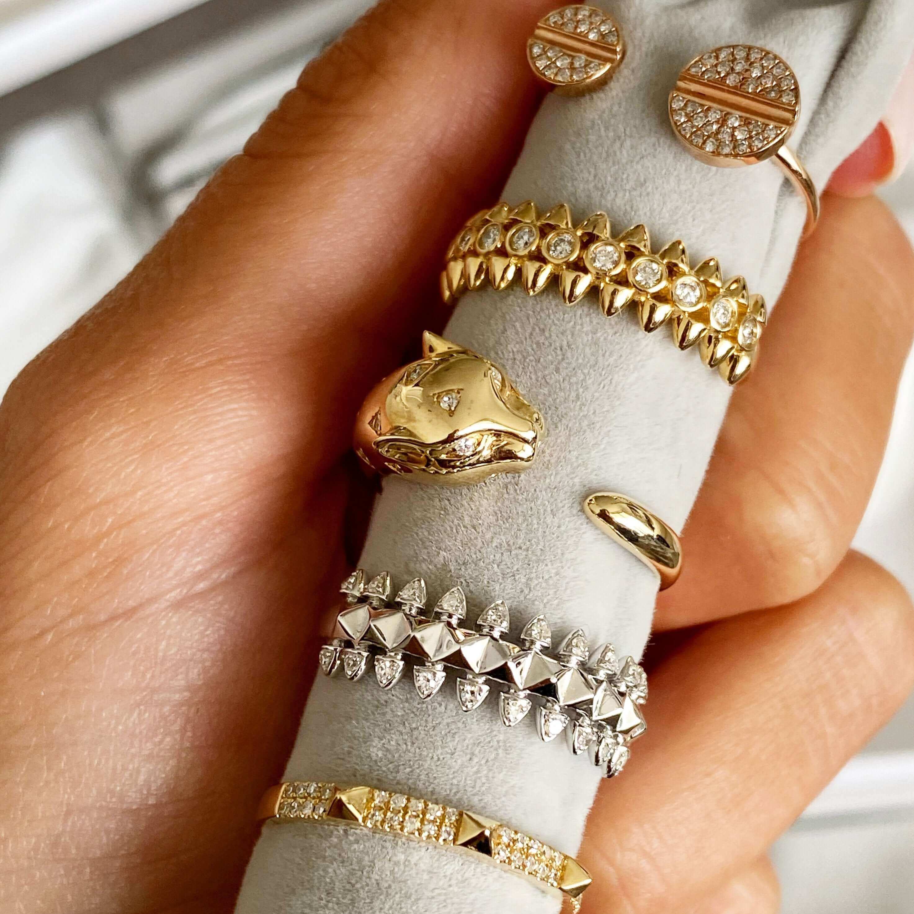 Hand holding a velvet ring holder showcasing a collection of gold and diamond-studded rings from our luxury jewelry brand