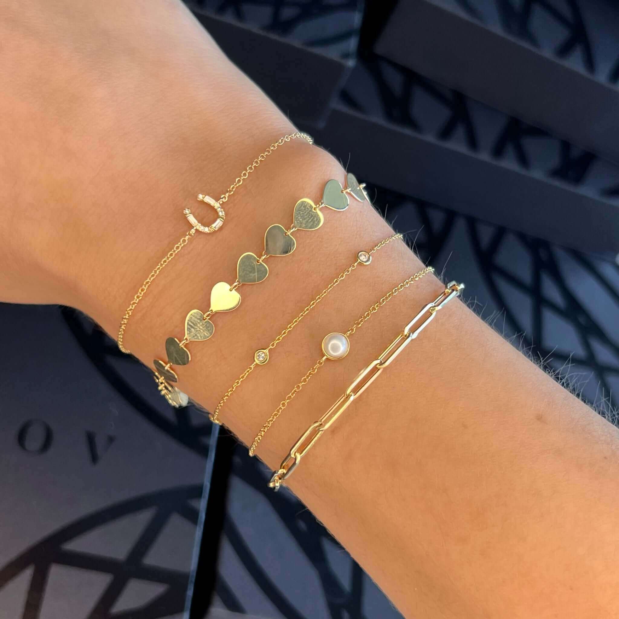 Woman's wrist adorned with trendy gold bracelets featuring hearts, charms, and pearls from our elegant jewelry collection.