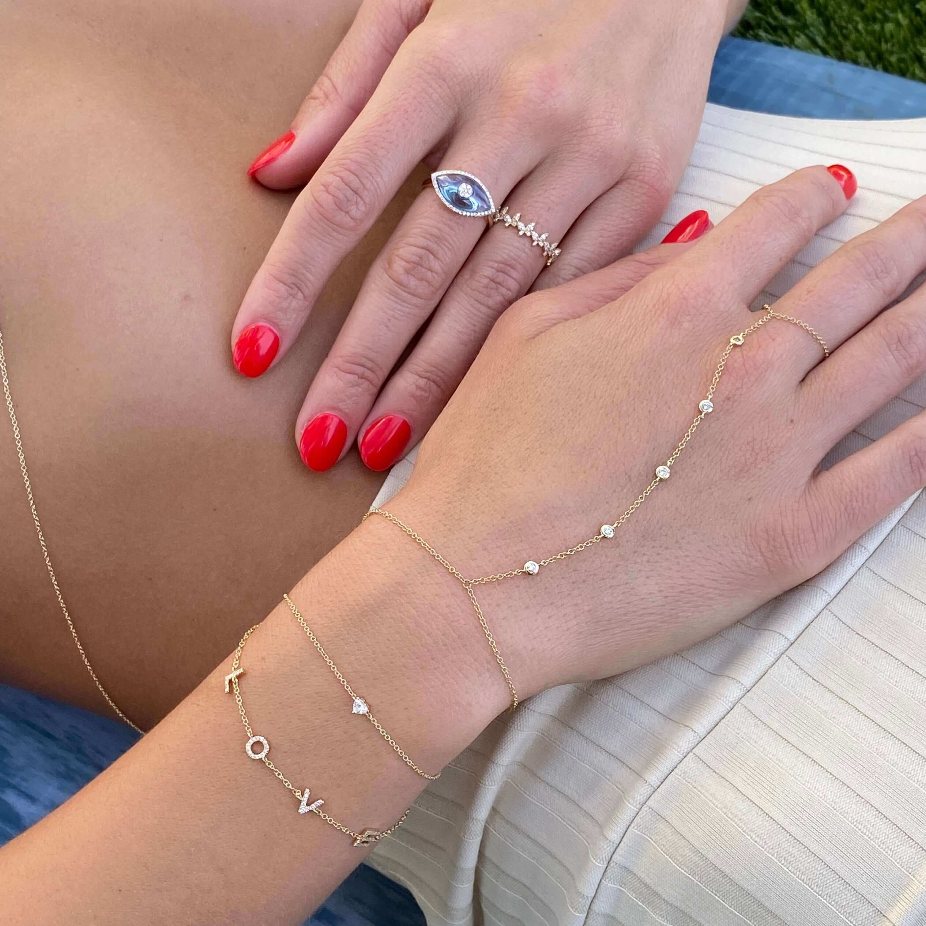 Elegant gold bracelets and a blue gemstone ring on hands with red nail polish from our unique jewelry collection.