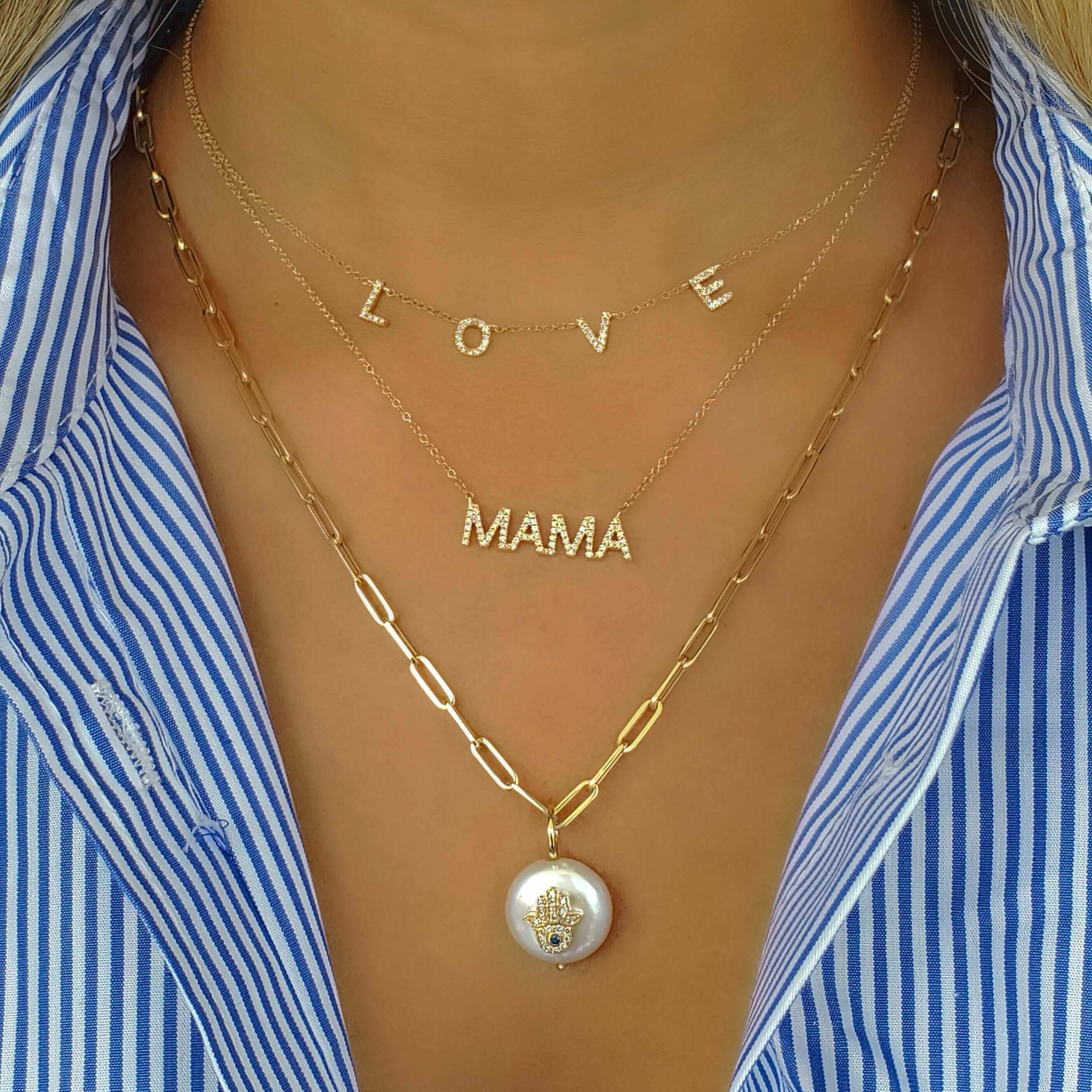 Woman wearing layered "LOVE," "MAMA," and gold chain necklaces with pendant, styled with a blue and white striped shirt.