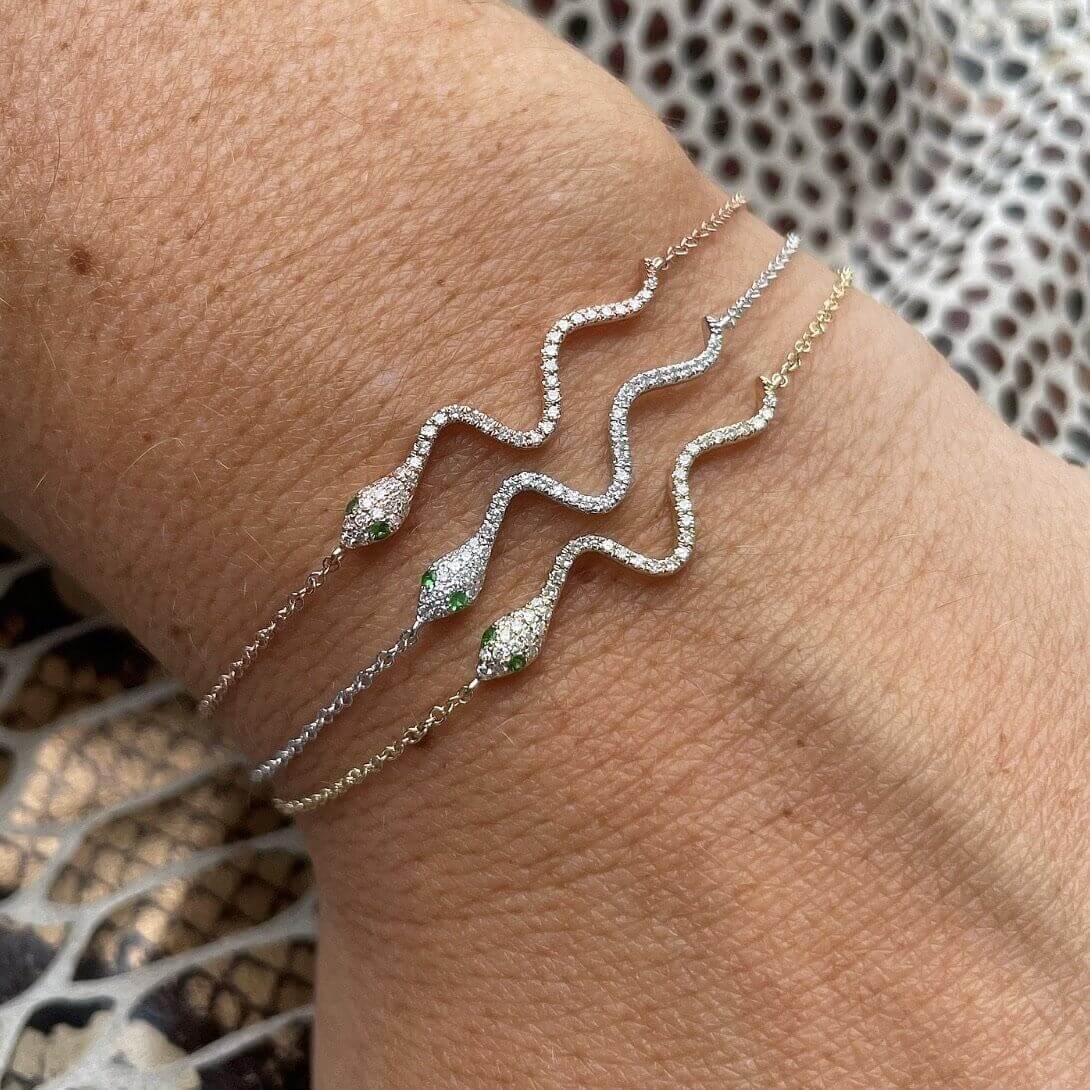 Elegant snake-chain bracelets with sparkling diamonds and green gemstones on a wrist, from our exclusive jewelry collection.