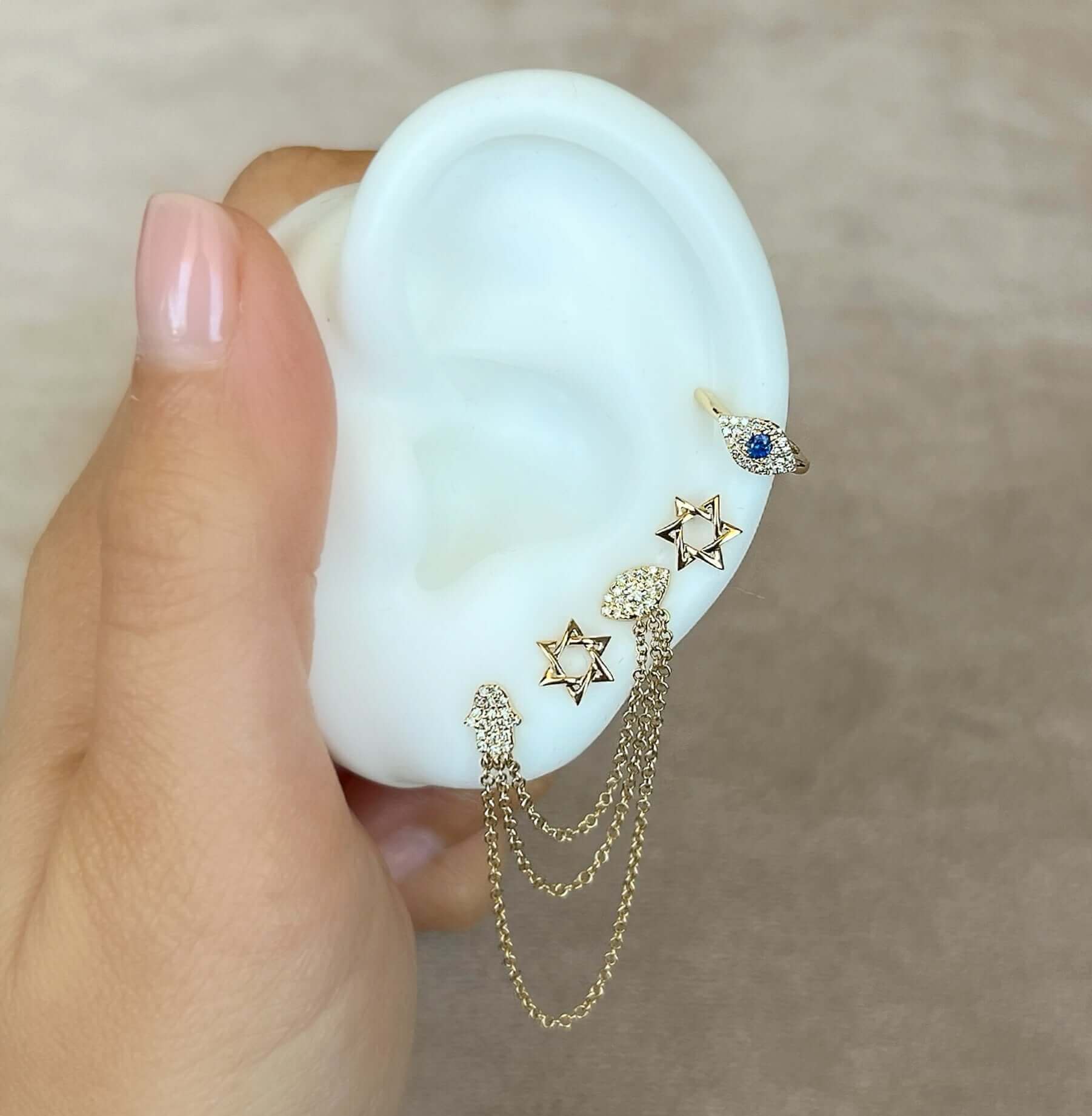 Hand holding a faux ear adorned with gold star and eye jewelry with chains from our jewelry brand collection