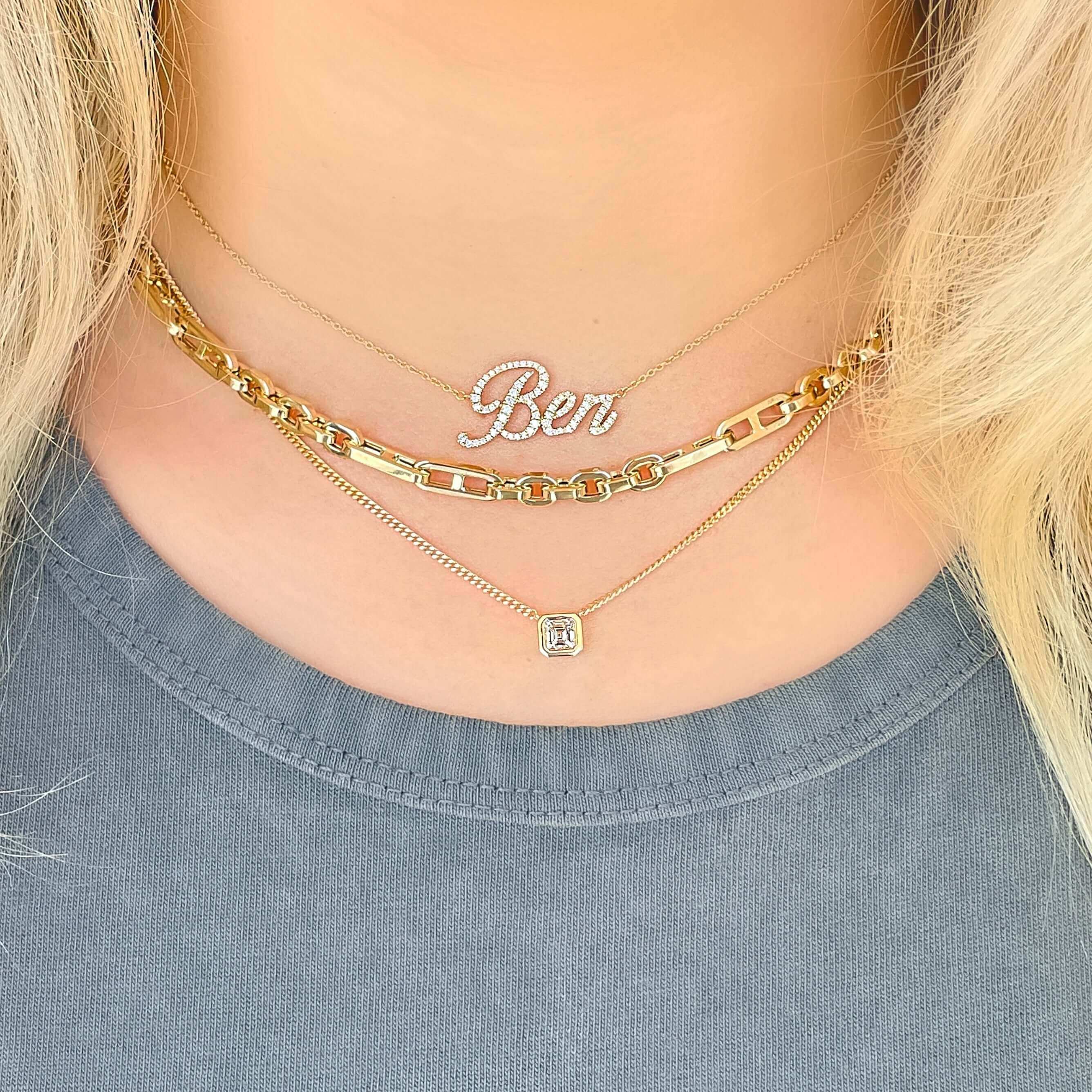 Woman wearing layered gold necklaces, including a personalized "Ben" name necklace and a square pendant necklace, by our jewelry brand.