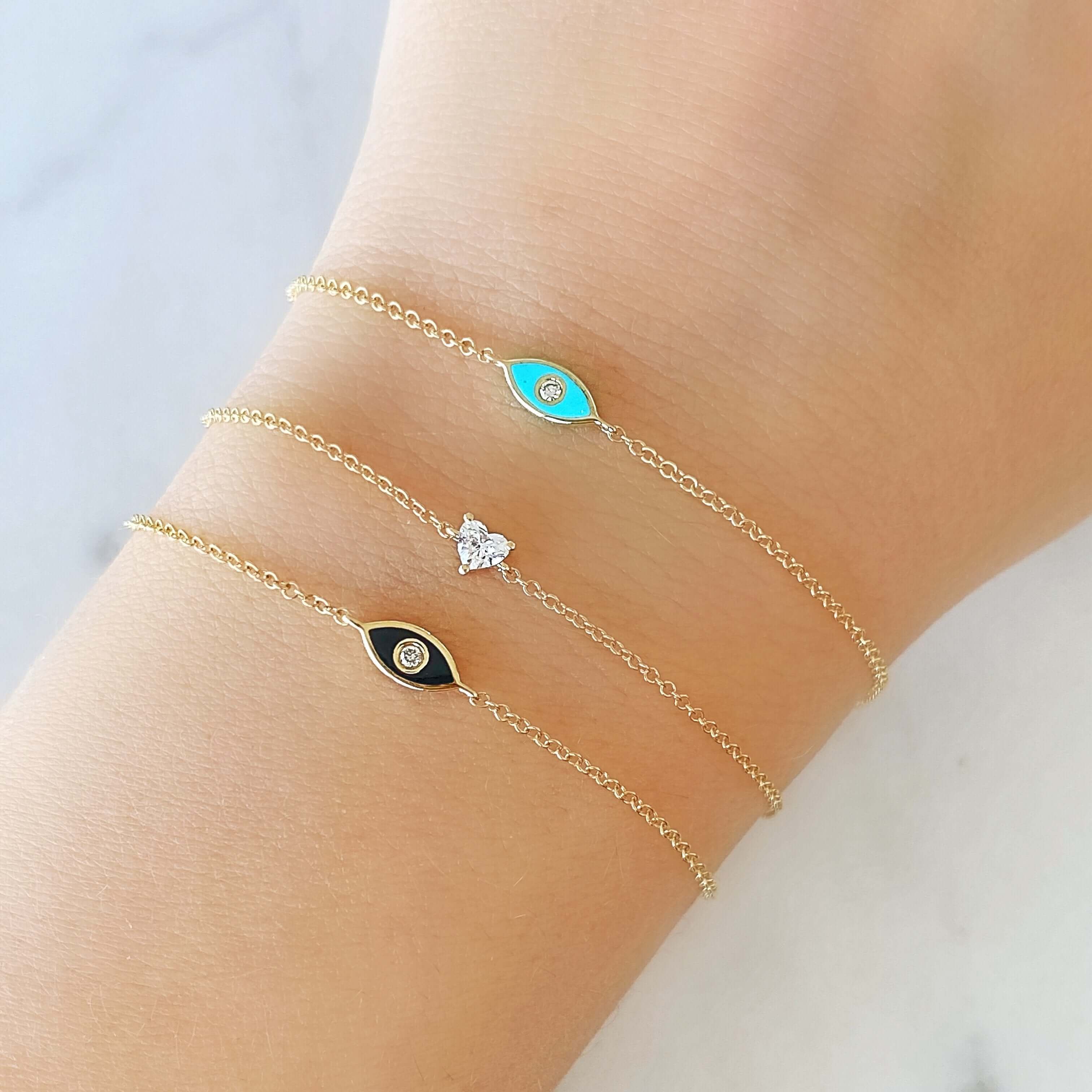 Delicate gold bracelets with black, blue, and white enamel evil eye charms, featured on a wrist from our jewelry collection.
