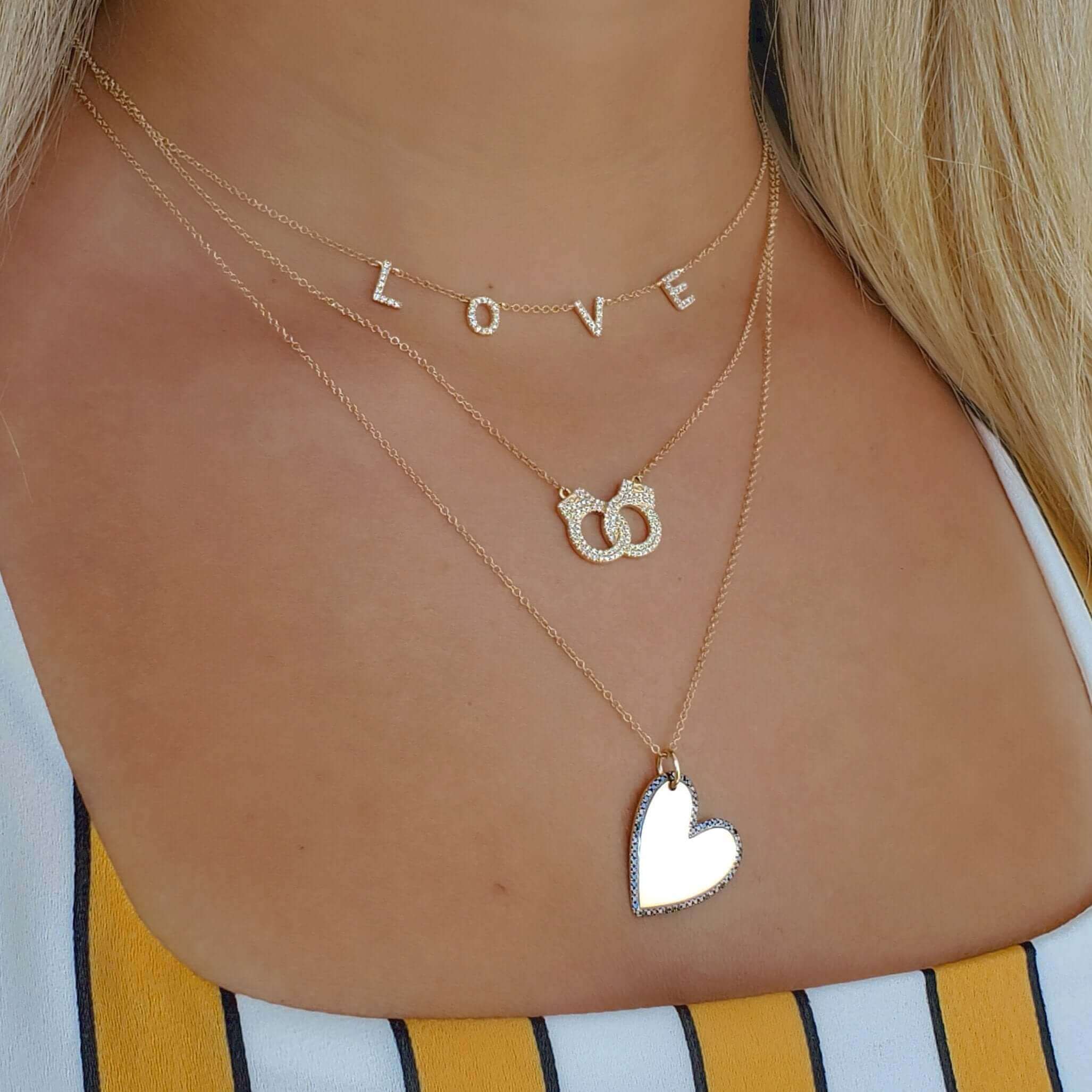 Woman wearing layered gold necklaces with love letters, intertwined rings, and a heart pendant from our jewelry collection