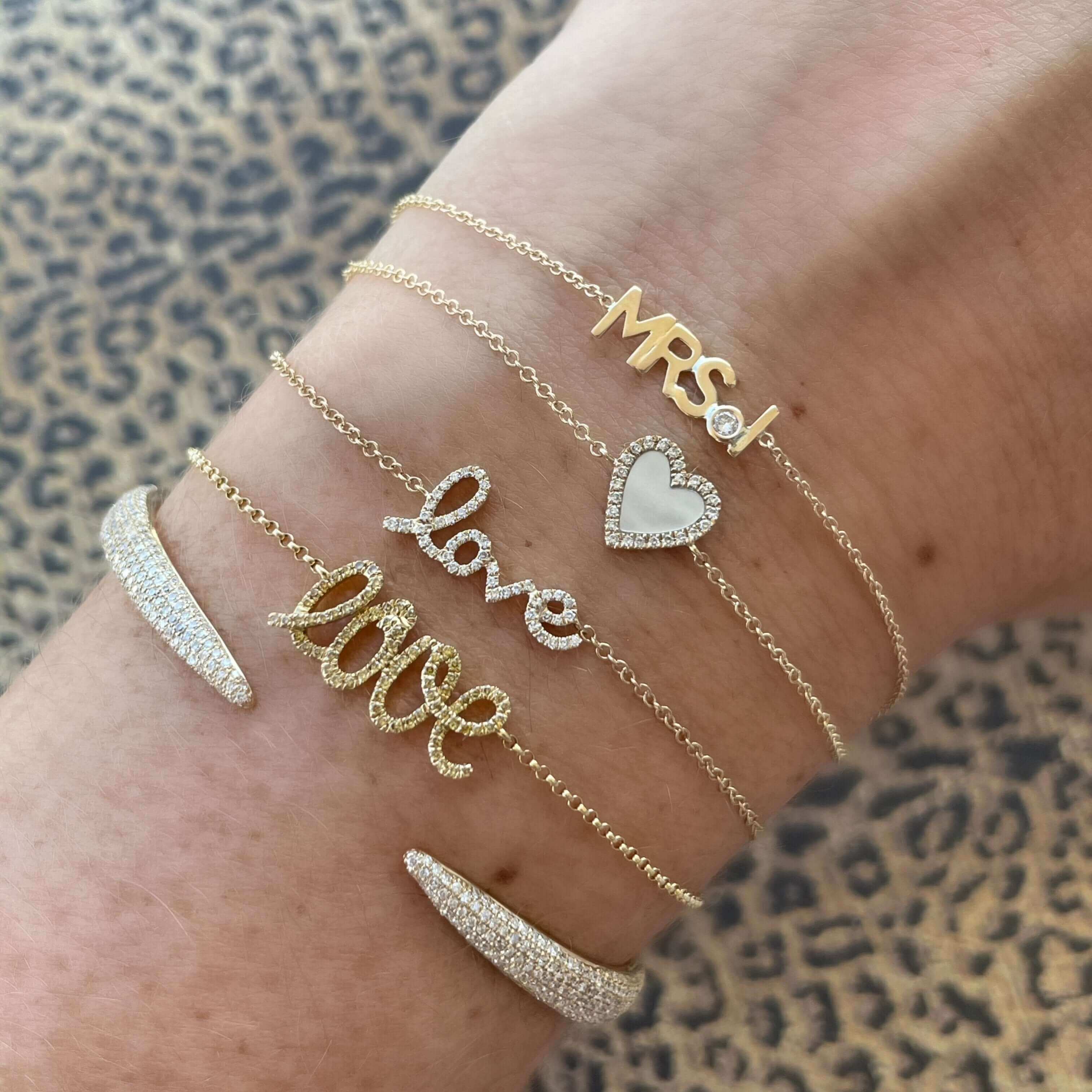 Delicate gold jewelry with "Mrs.", "love", and heart charms on a wrist with a leopard print background