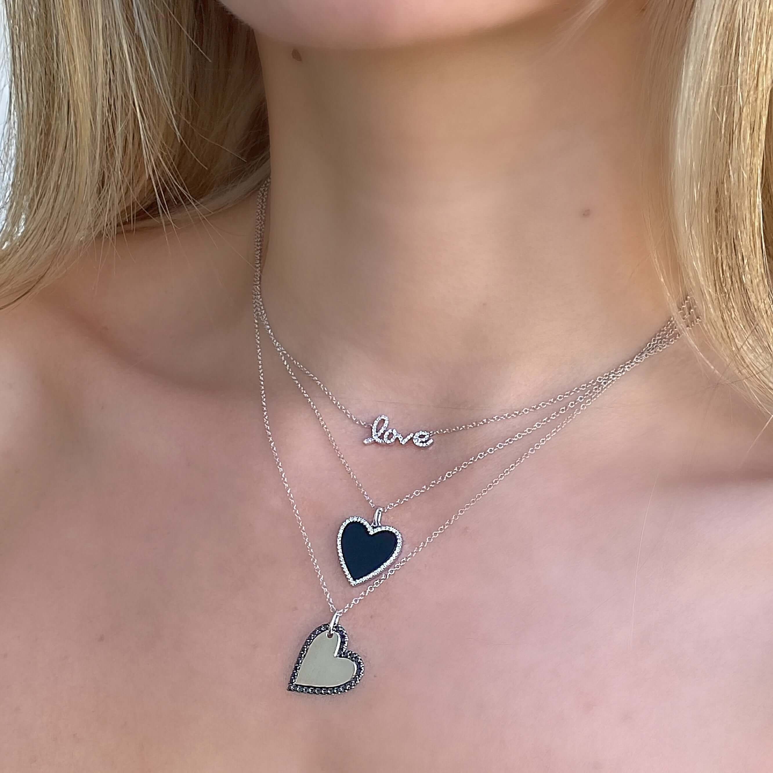 Woman wearing layered heart necklaces from our jewelry brand, featuring a "love" pendant and elegant silver chains.