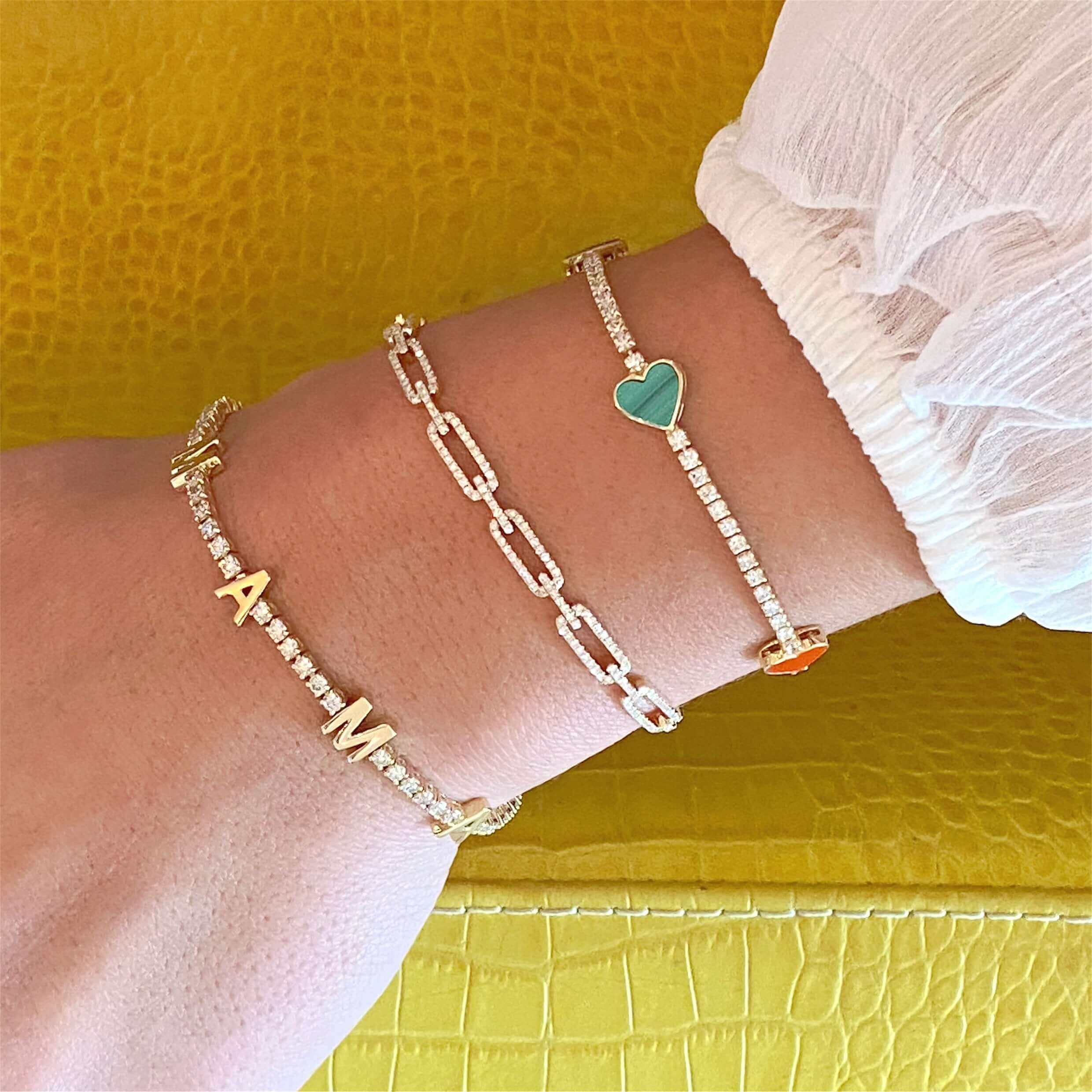 Gold and diamond bracelets with initial letters and heart charm showcased on a yellow background by our luxury jewelry brand.