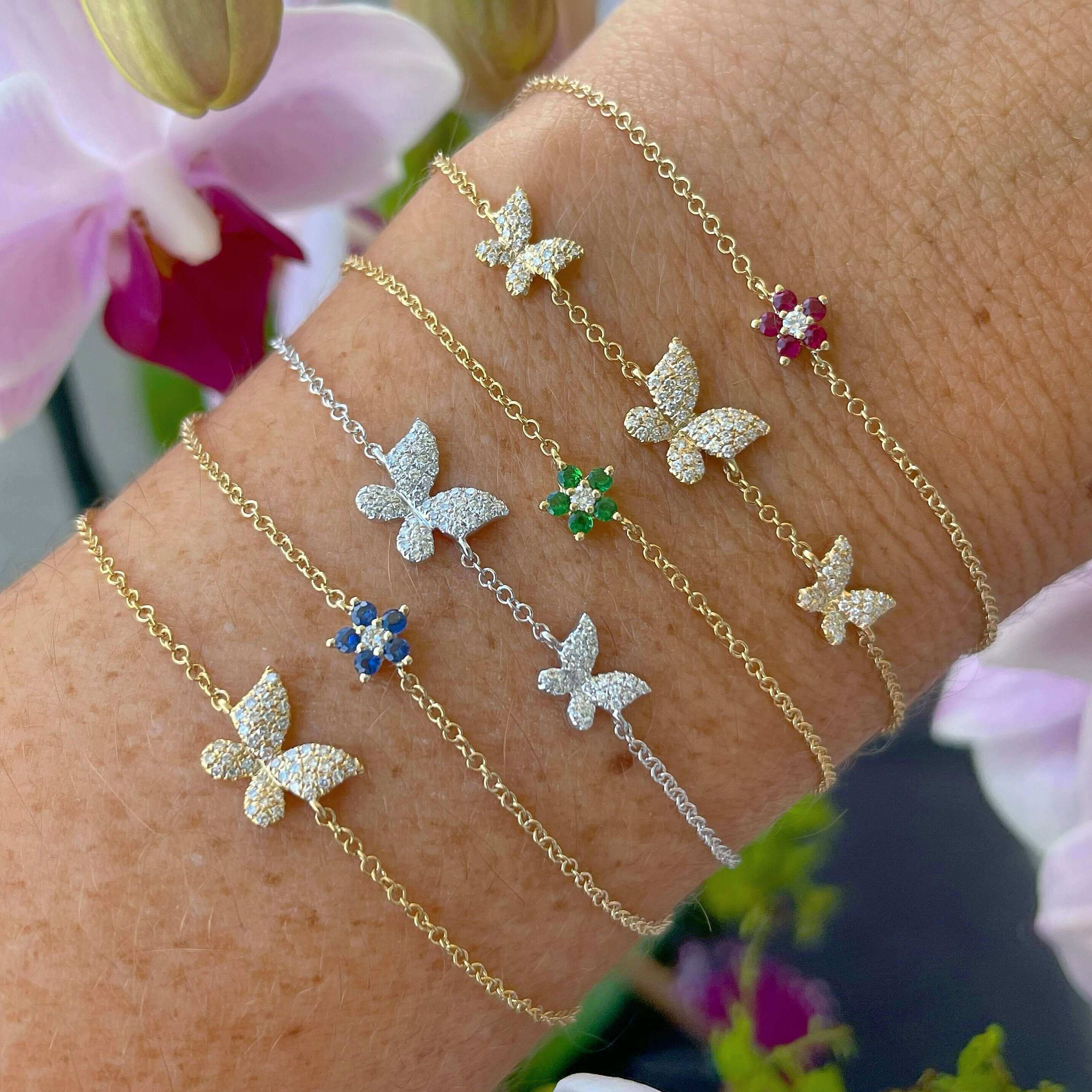 Butterfly charm bracelets in various colors from our jewelry collection displayed on a wrist with a floral backdrop.
