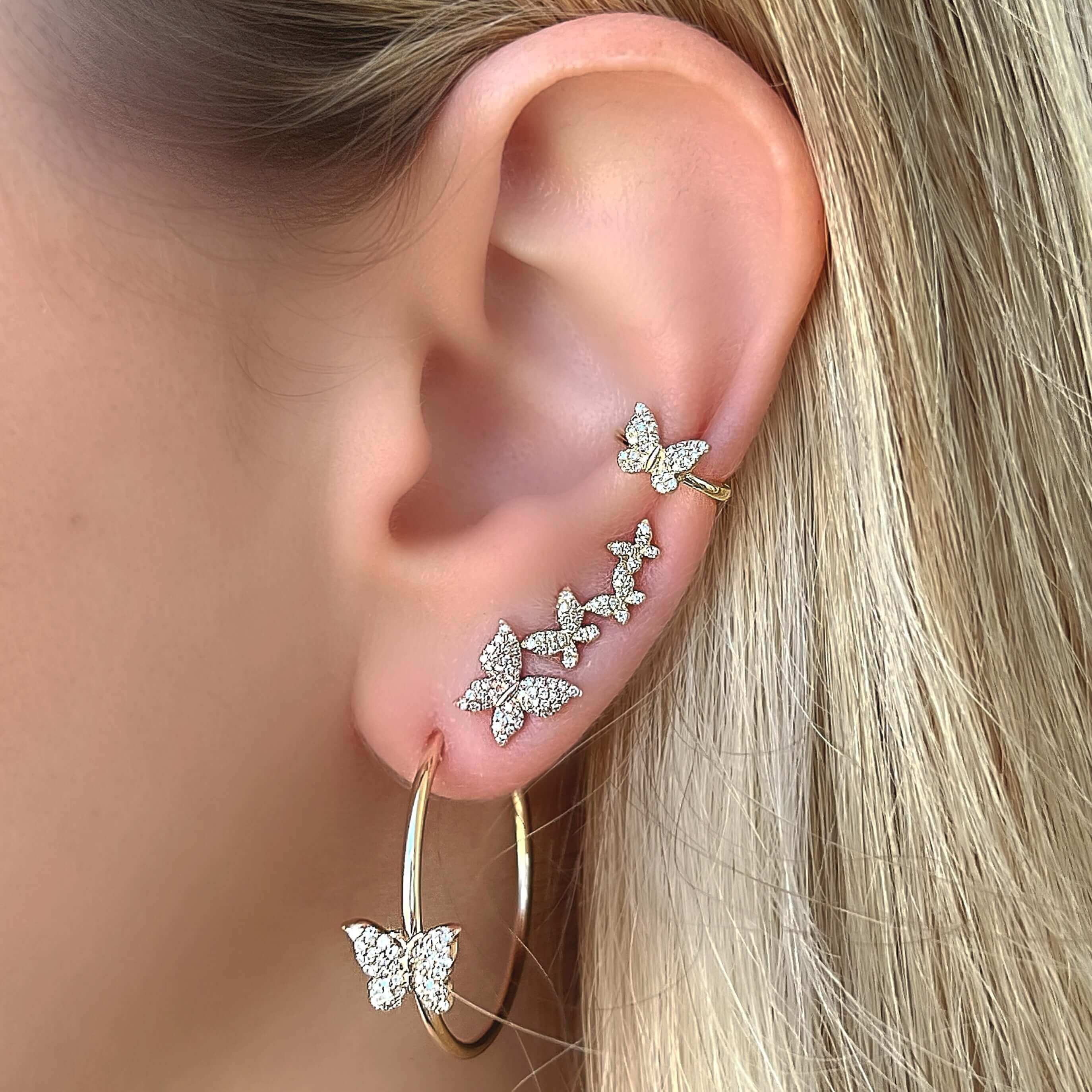 Woman's ear adorned with elegant butterfly-themed gold hoop and ear climber earrings sparkling with diamonds from our jewelry collection.