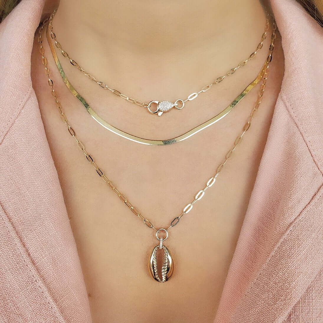 Woman wearing layered gold necklaces featuring a seashell pendant and intricate chain designs from our jewelry collection