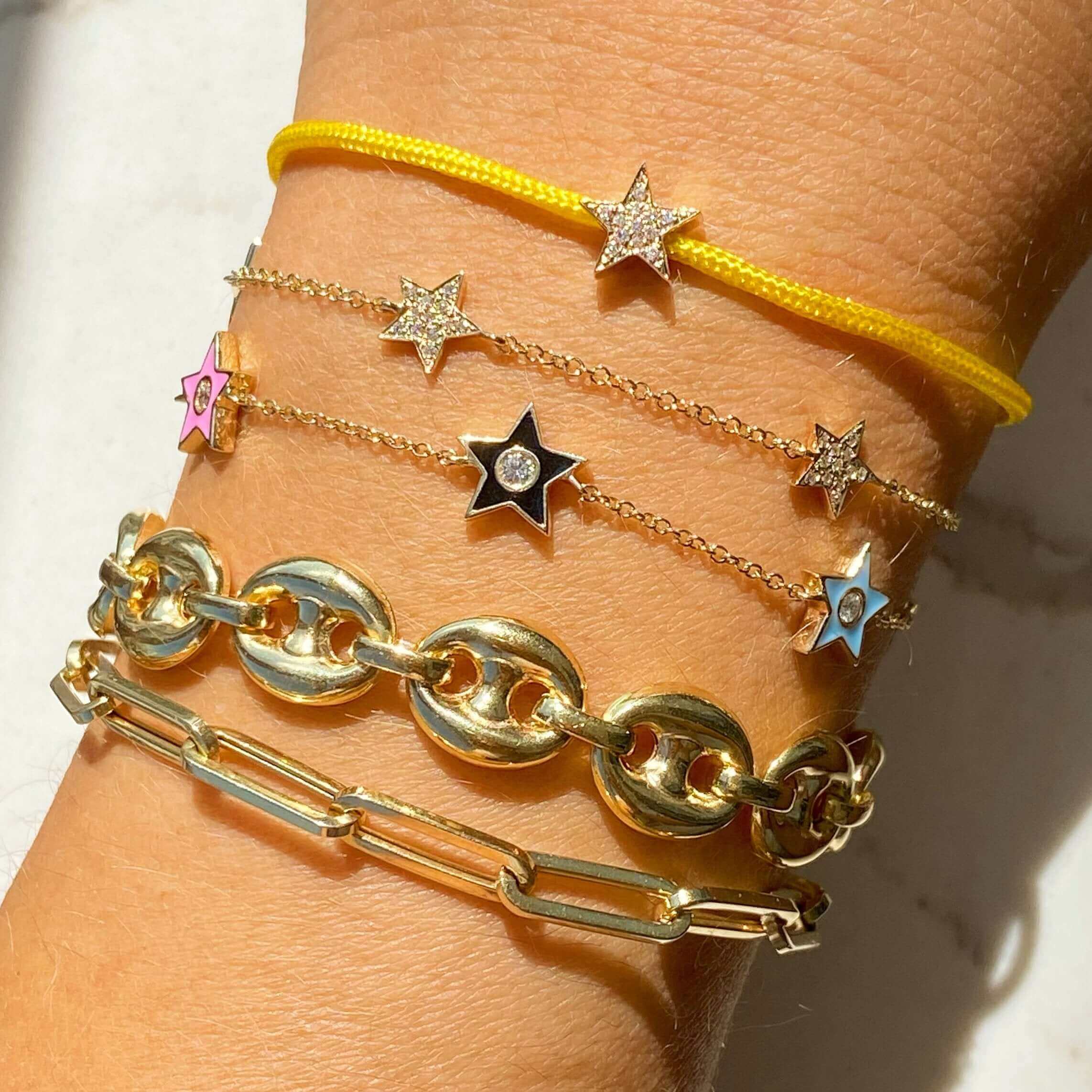 Woman's wrist adorned with star-themed bracelets and gold chain bracelets showcasing jewelry brand's collection.