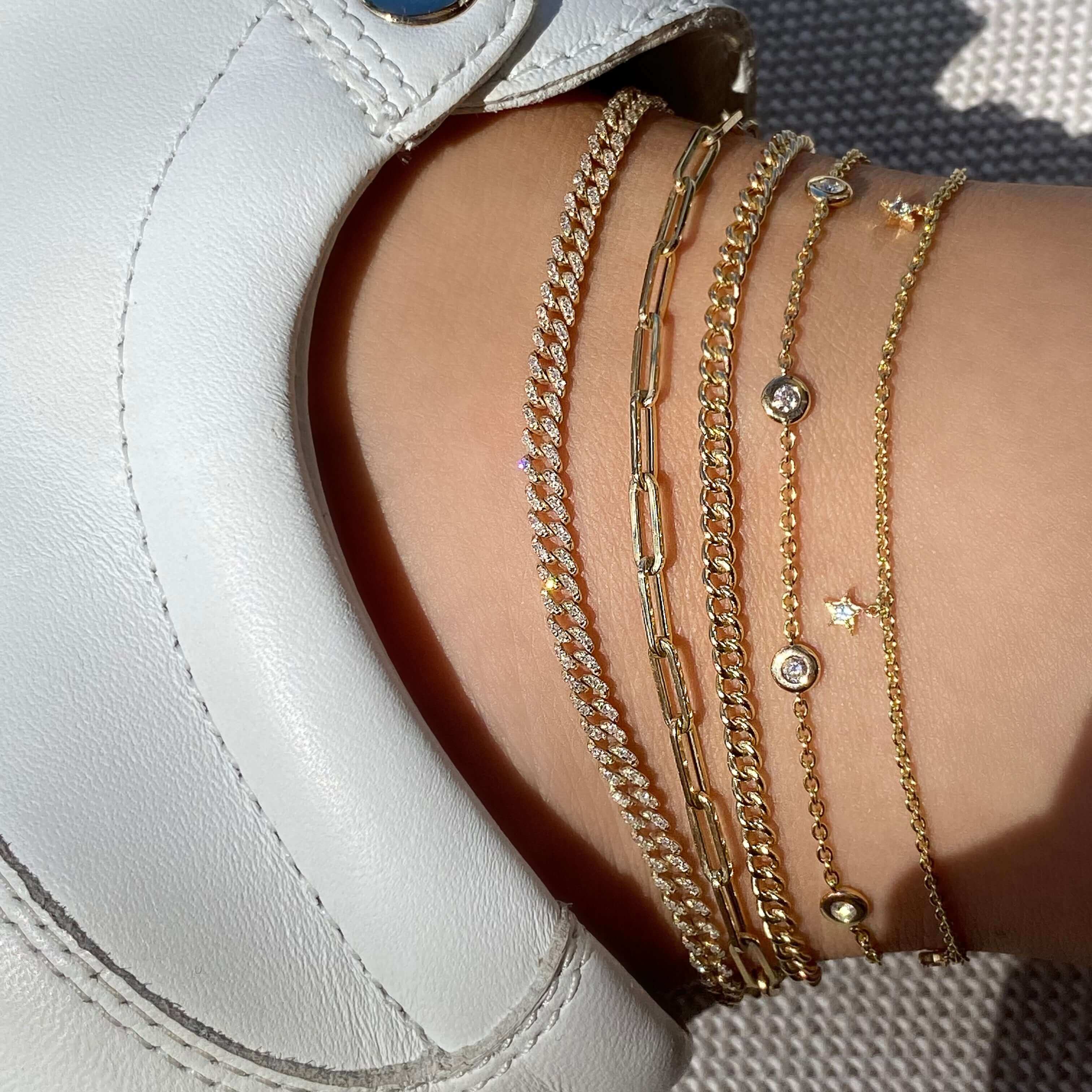 Elegant gold anklets from our jewelry brand, showcased against white shoes, featuring delicate diamond accents and intricate chain designs.