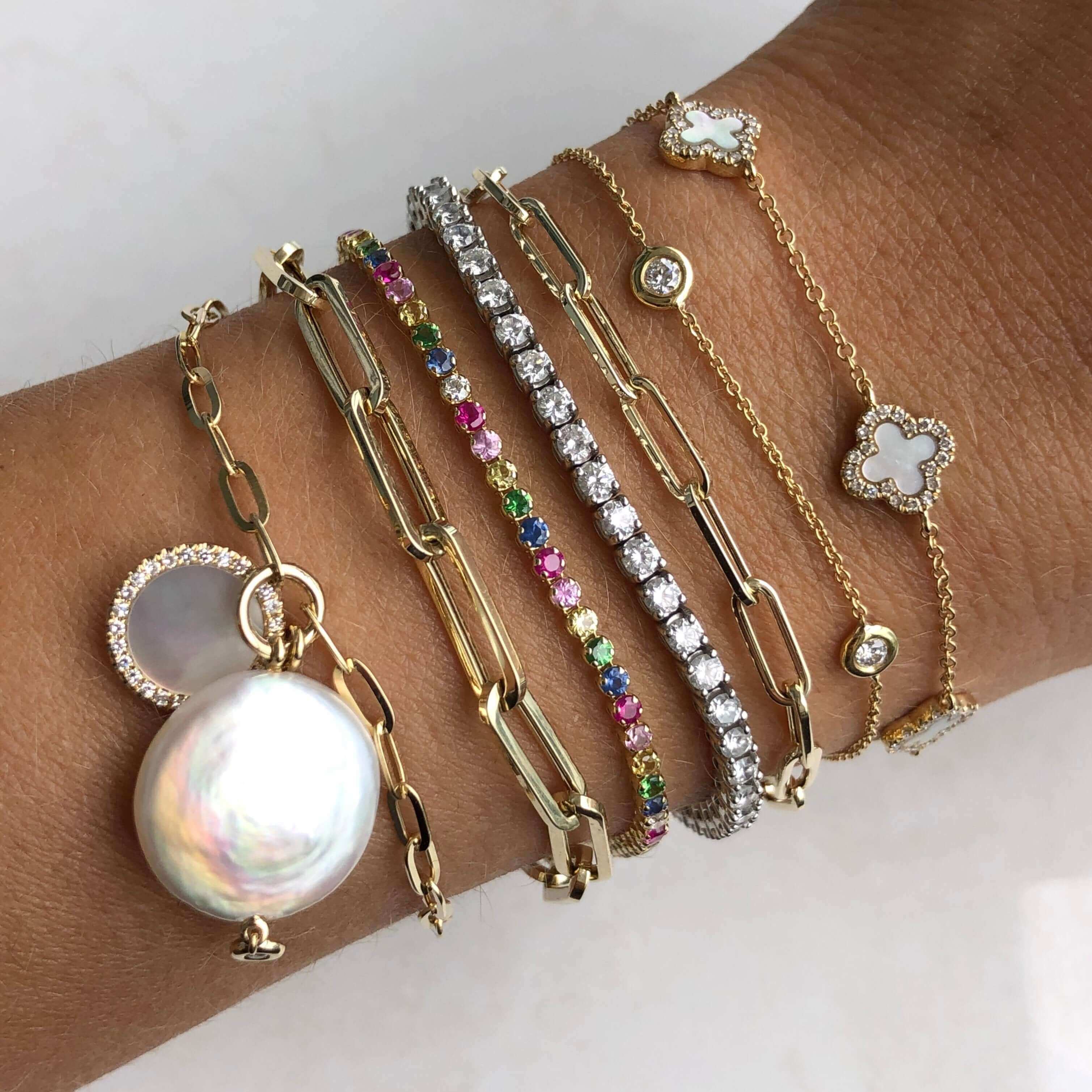 Elegant stack of gold bangles featuring pearls, colorful gemstones, and diamond accents from our luxurious jewelry brand collection.