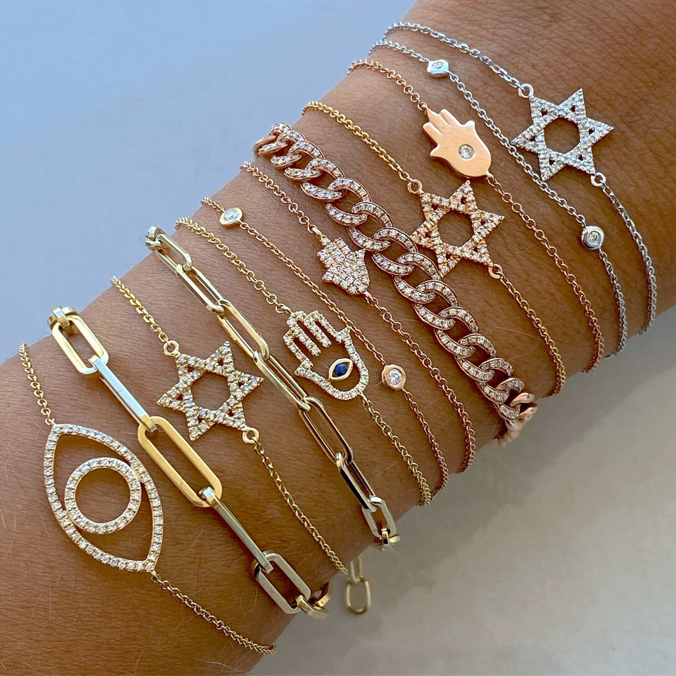 Stack of delicate gold and silver bracelets featuring star and evil eye charms, from our elegant jewelry collection.