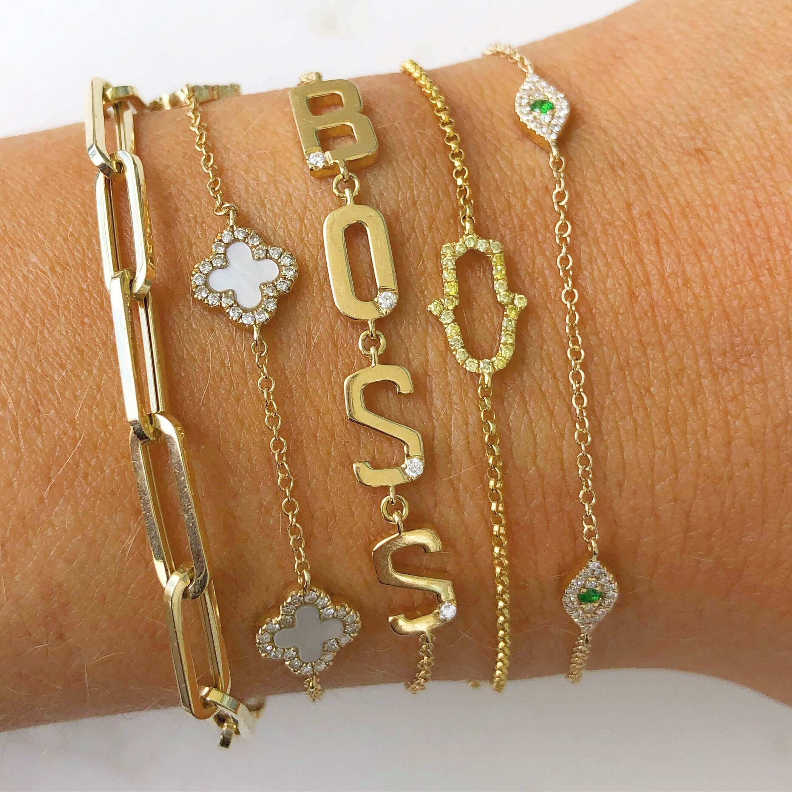 Gold and diamond bracelet stack featuring letters spelling "BOSS" and intricate designs from our luxury jewelry collection.