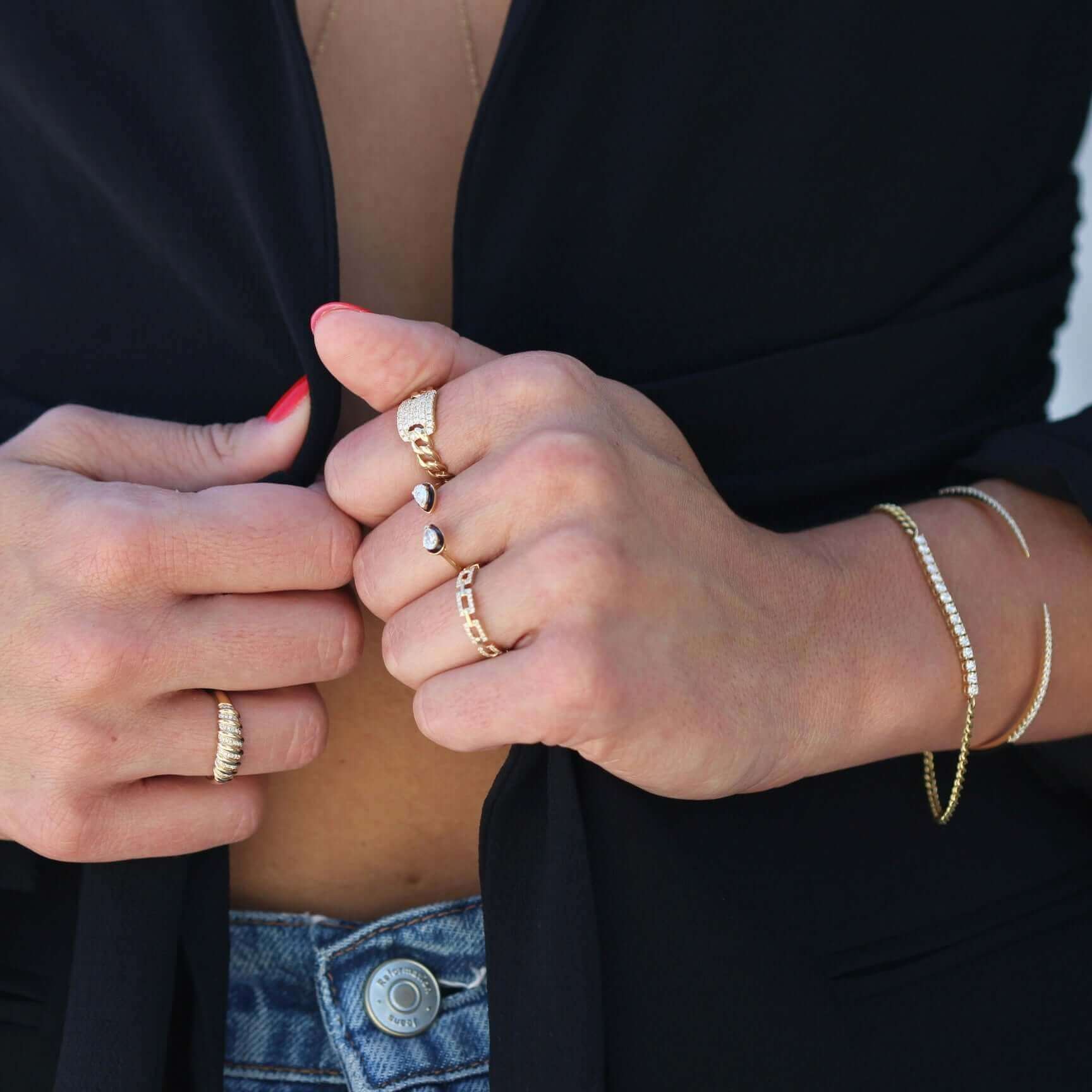Woman showcasing elegant gold rings and bracelets from our jewelry collection, wearing a black top and jeans.