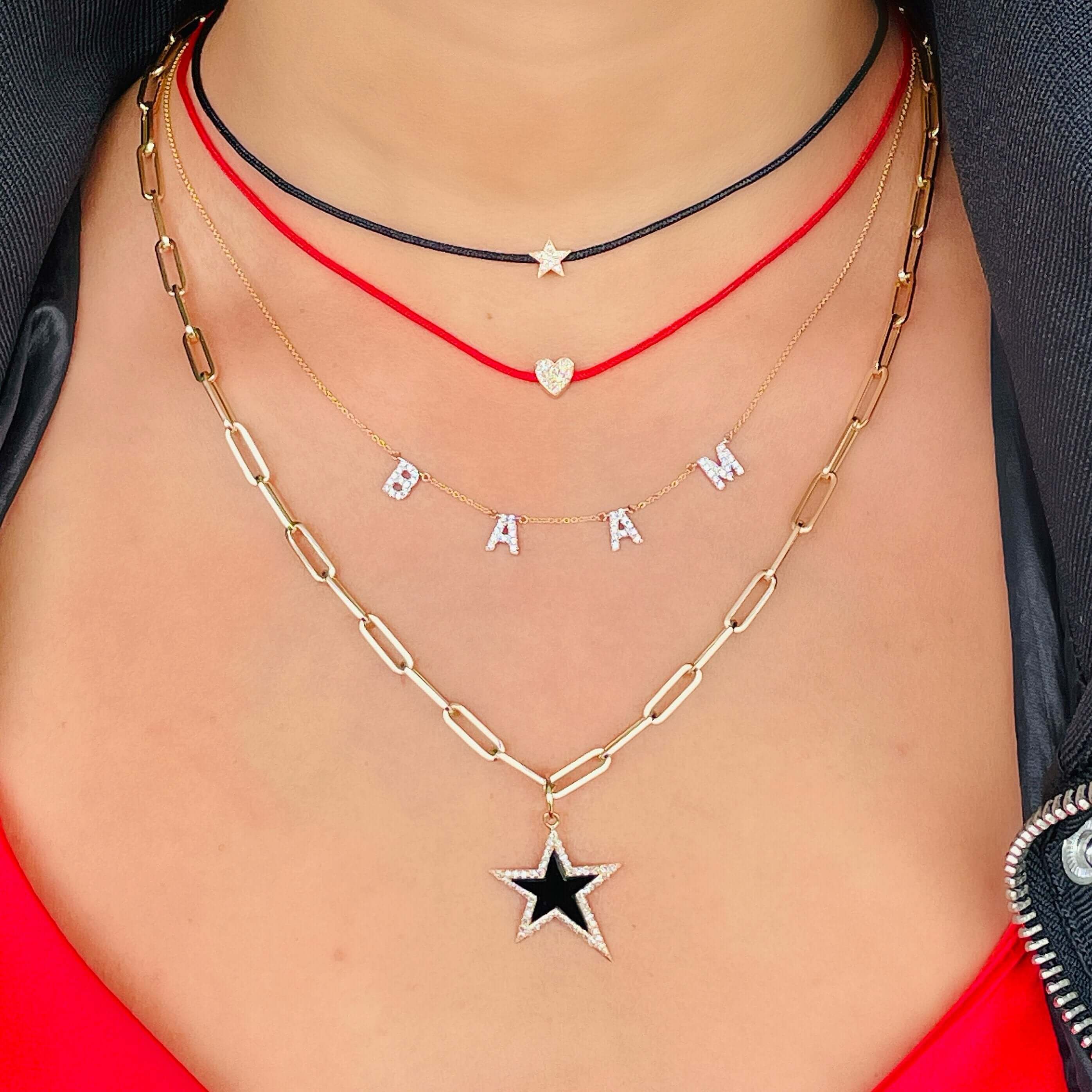 Stylish layered jewelry featuring a black star pendant and personalized letter necklaces, perfect for a bold and trendy look.