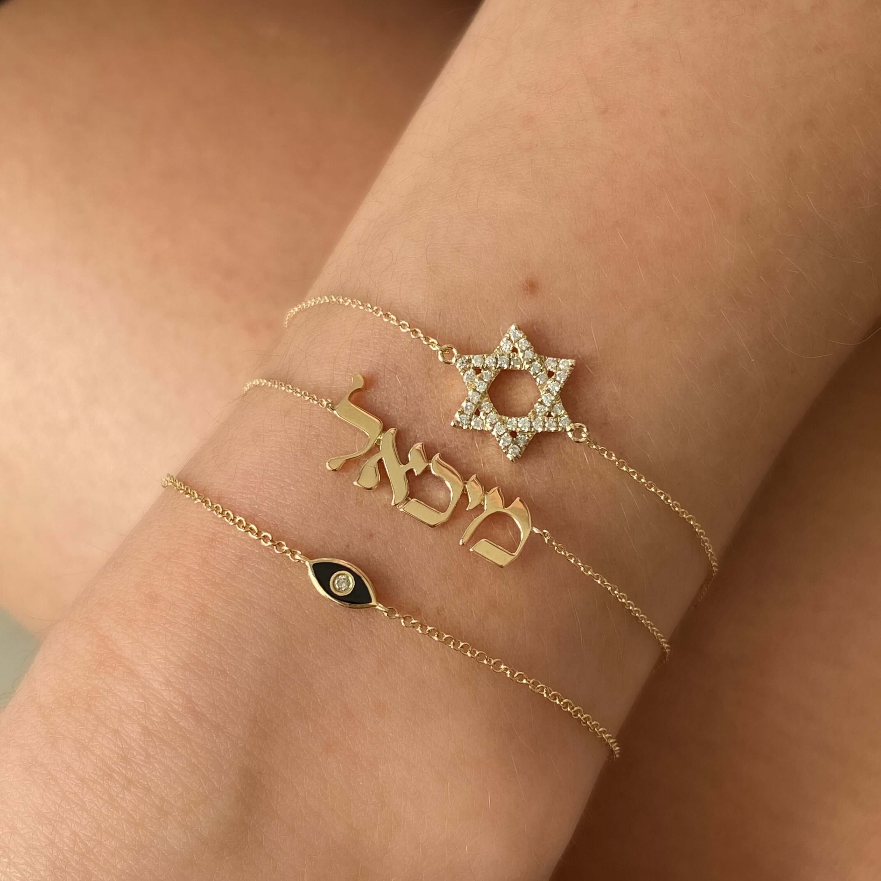 Gold bracelets featuring a star of David, Hebrew name, and an eye charm, elegant jewelry from our exclusive collection.