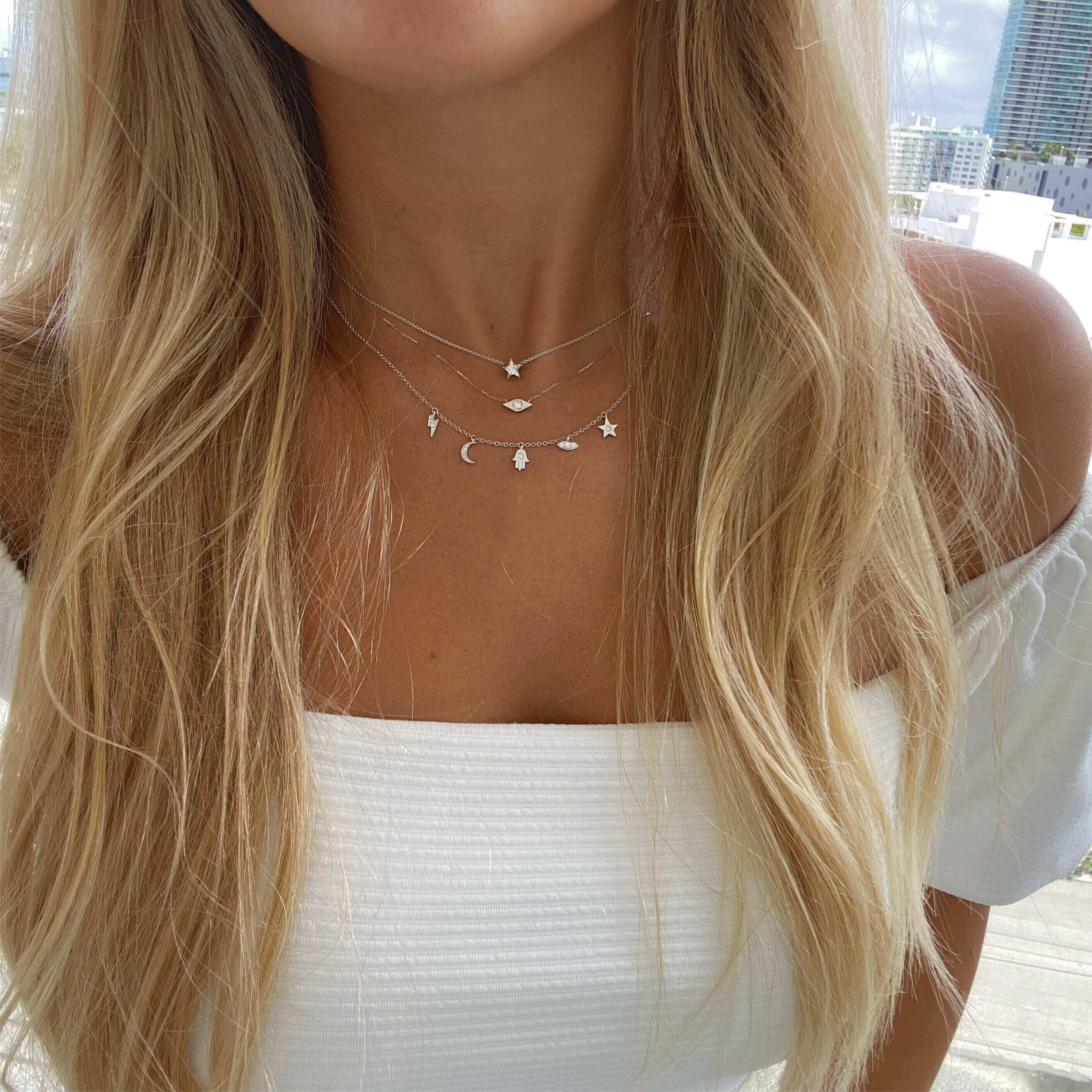 Woman wearing layered celestial-themed necklaces from our jewelry brand, featuring star and moon pendants, in a white off-the-shoulder top.