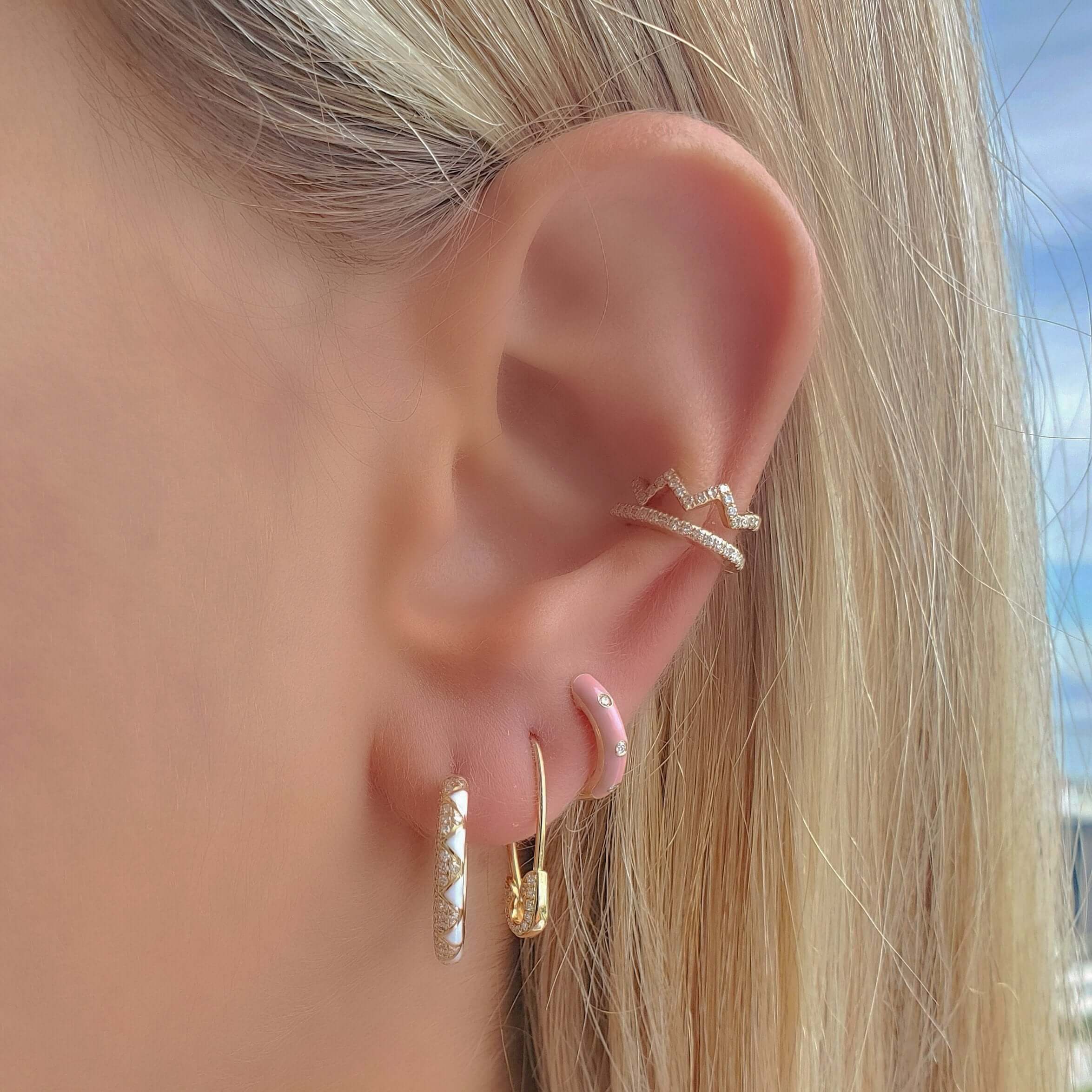 Ear adorned with multiple gold and diamond earrings, including a cuff, showcasing elegant jewelry from our premium collection against a blue sky background