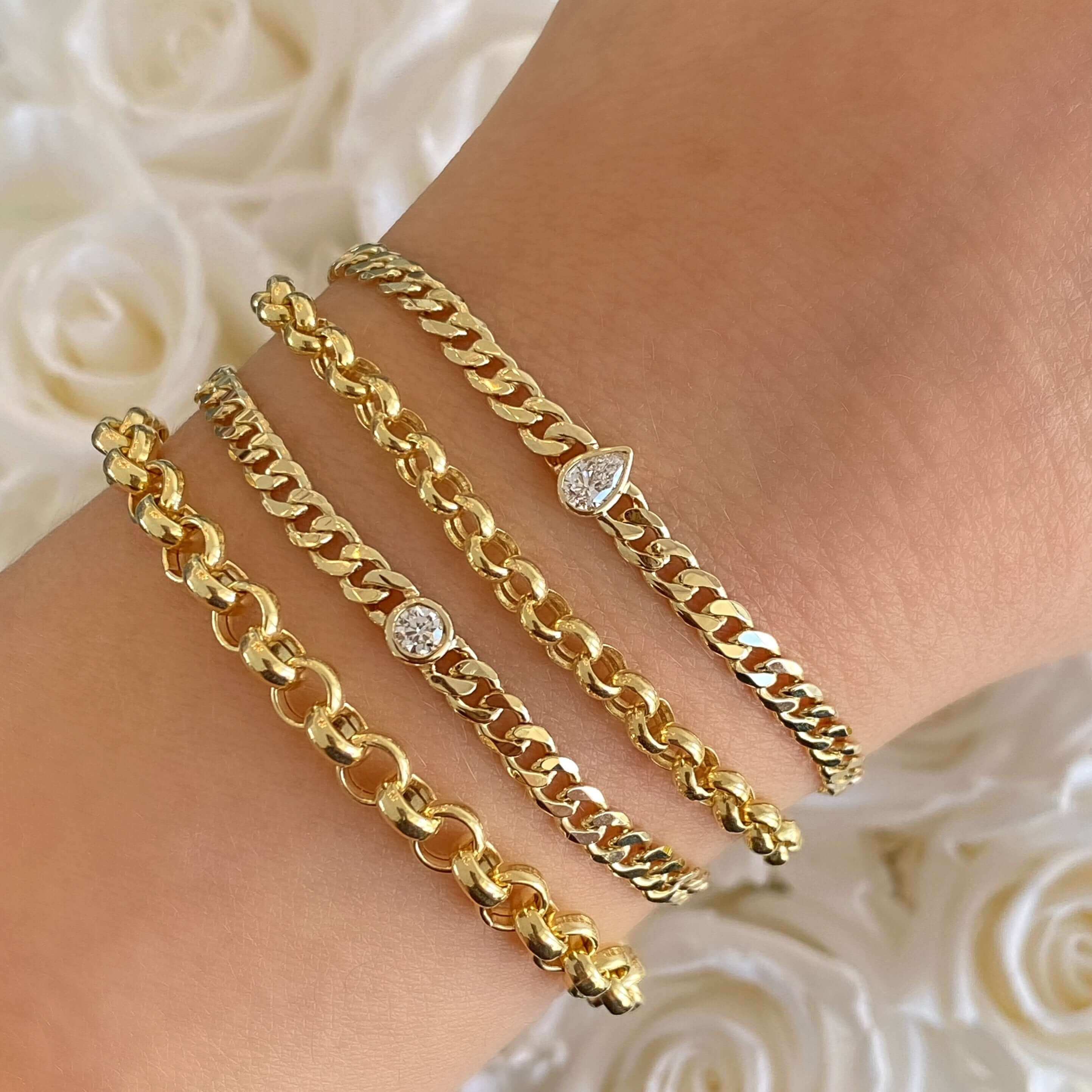 Elegant gold chain bracelets with diamond accents displayed on wrist, showcasing luxurious jewelry style against a white rose background.