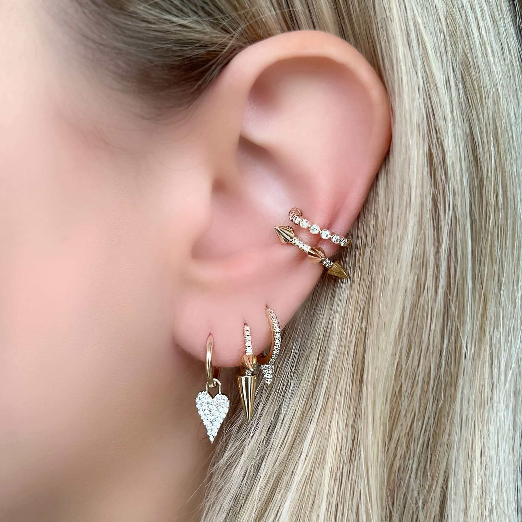 Woman wearing multiple gold and diamond earrings from our jewelry collection, featuring heart and arrow designs.
