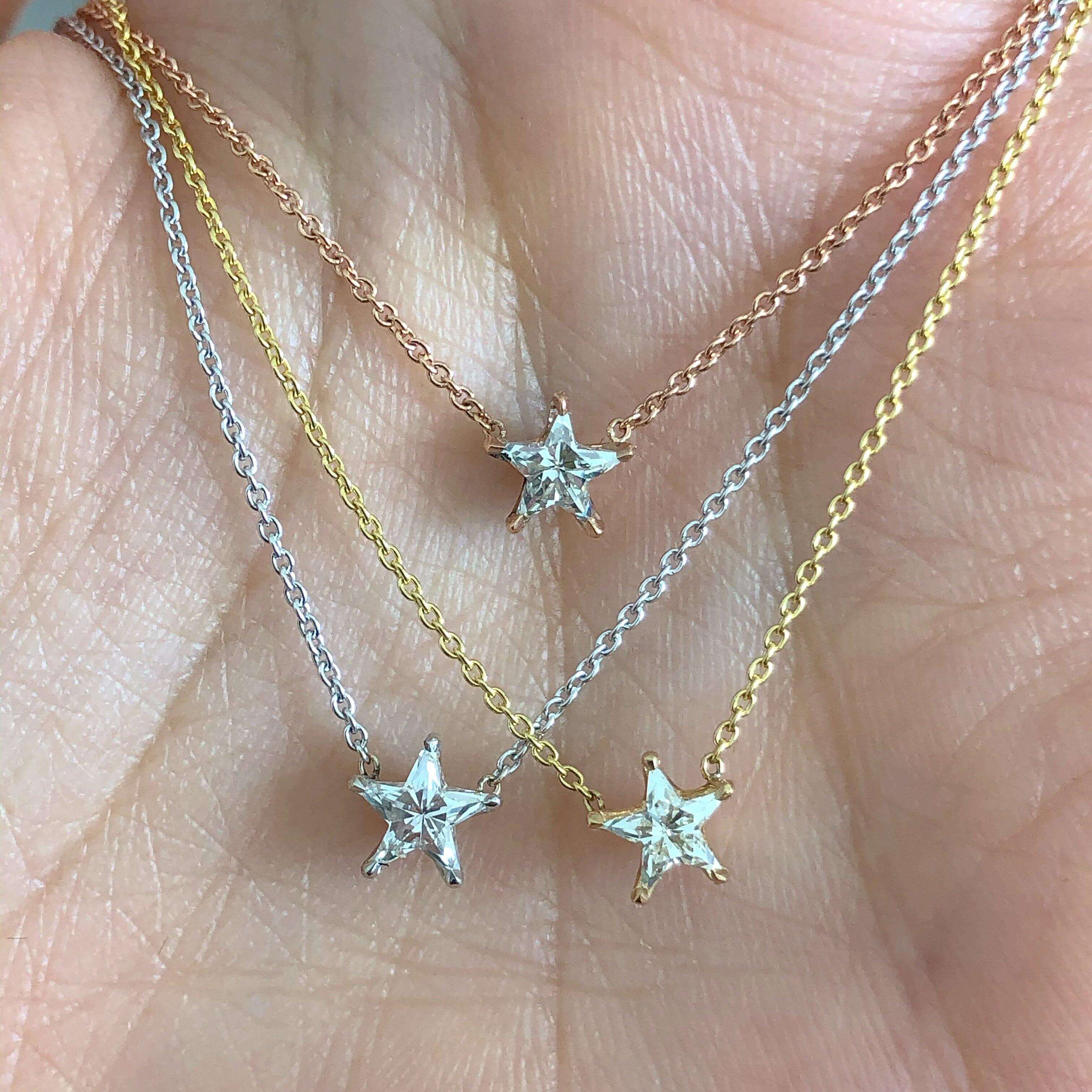 Hand displaying gold, silver, and rose gold star necklaces from our jewelry brand collection
