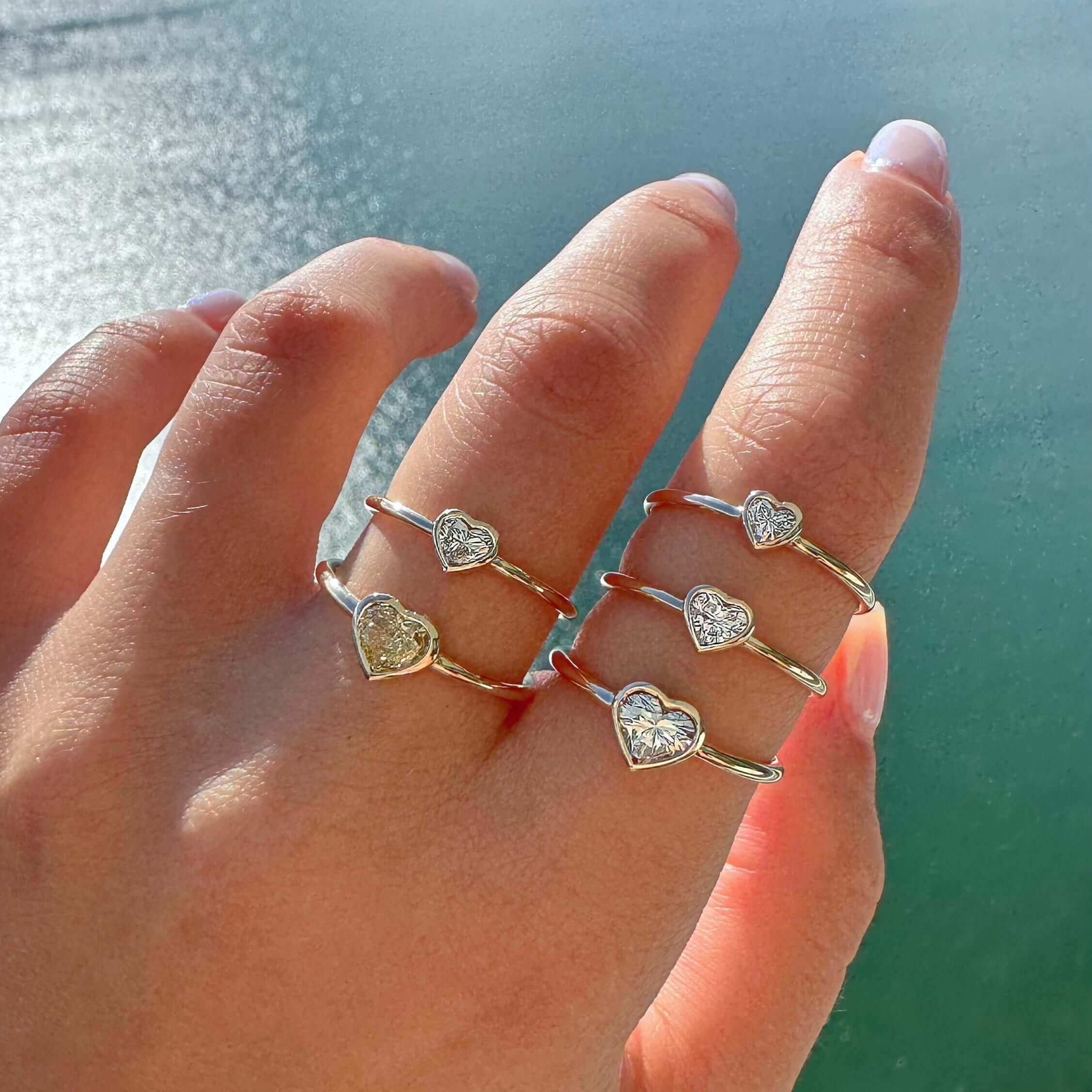 Bezel Set Natural Diamond Solitaire Ring displayed on fingers showcasing heart-shaped designs with a sparkling finish.