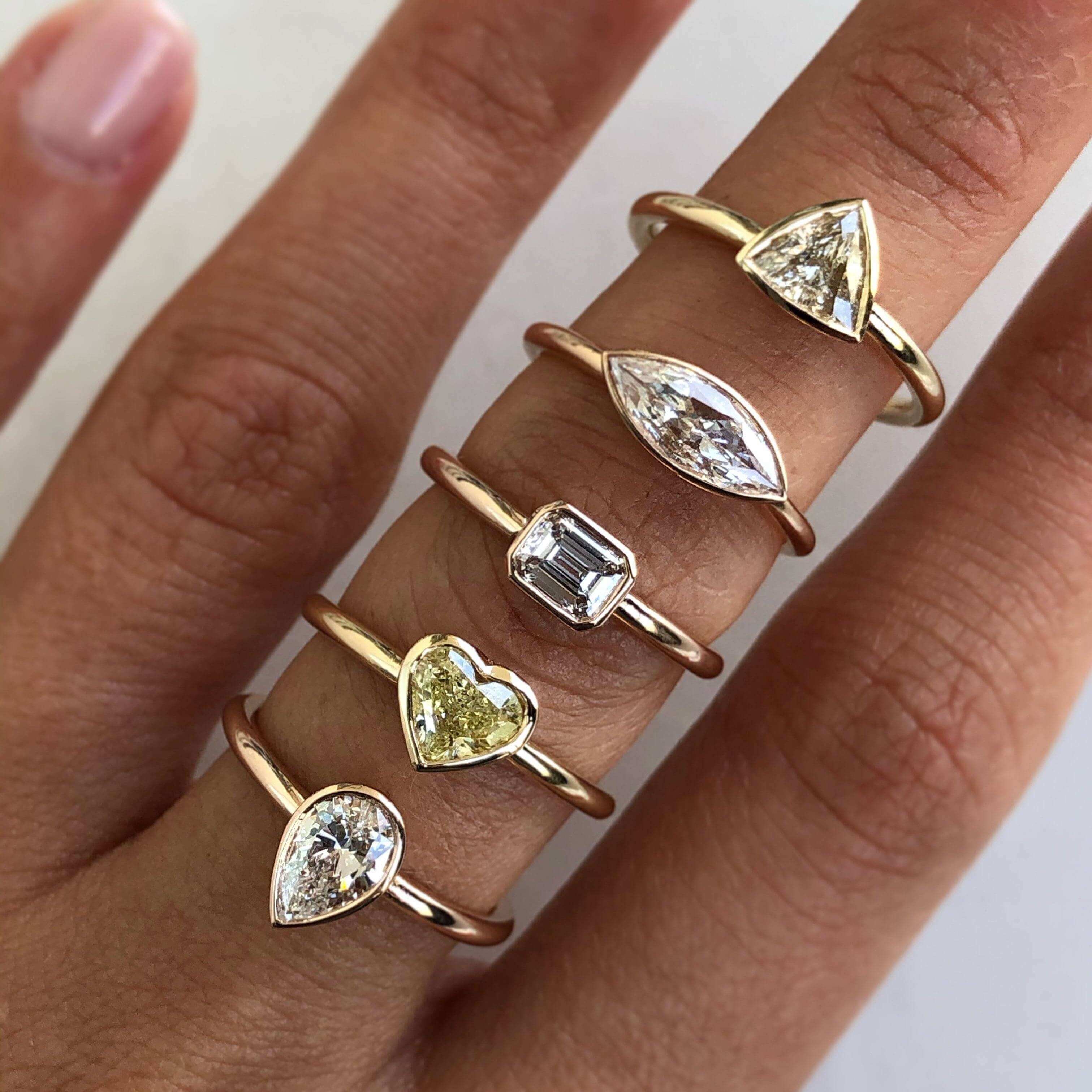 Elegant gold rings with various diamond shapes, including pear, heart, emerald-cut, marquise, and kite shape, showcased on a hand