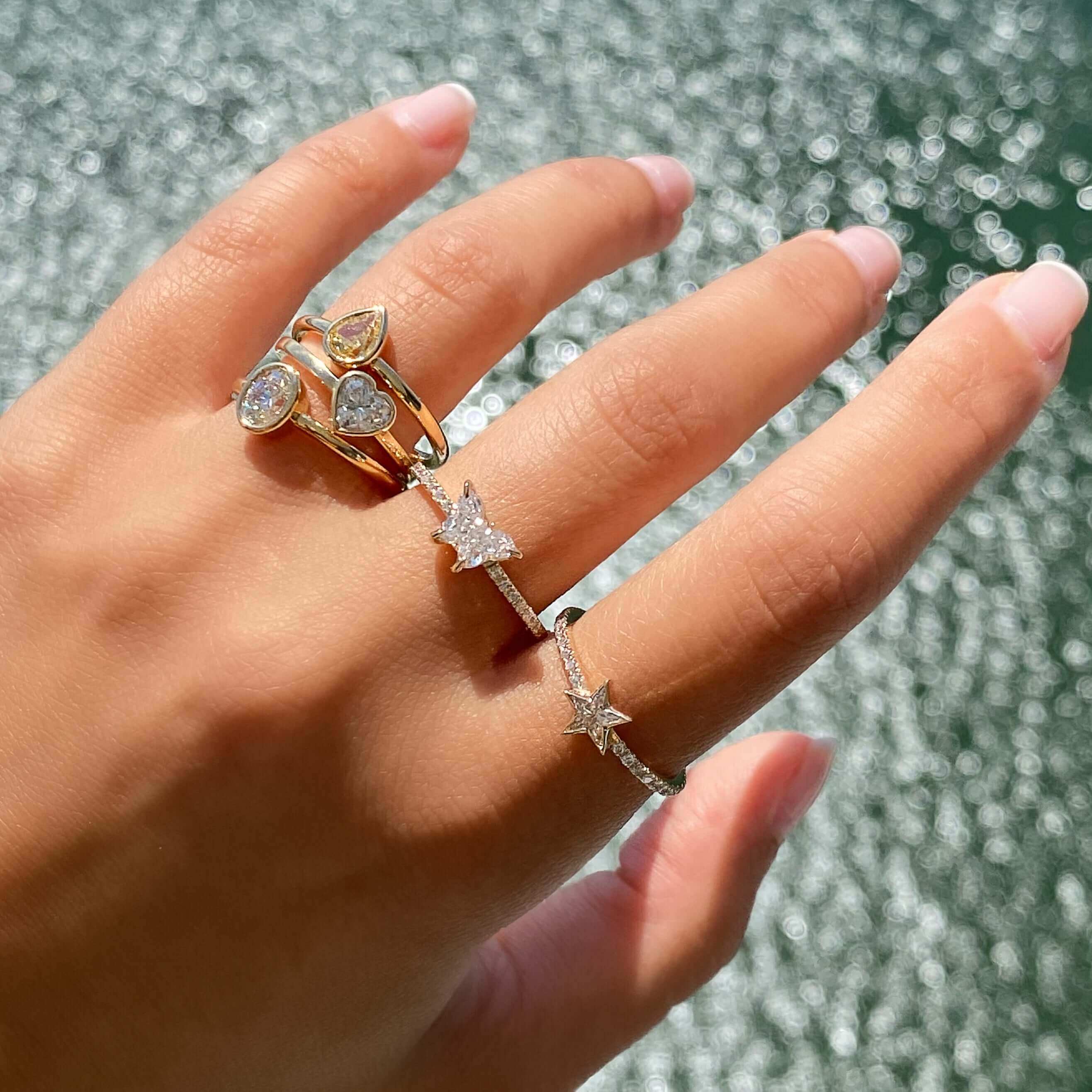 Hand adorned with luxurious star-shaped and teardrop diamond rings from our exclusive jewelry collection against a shimmering water backdrop