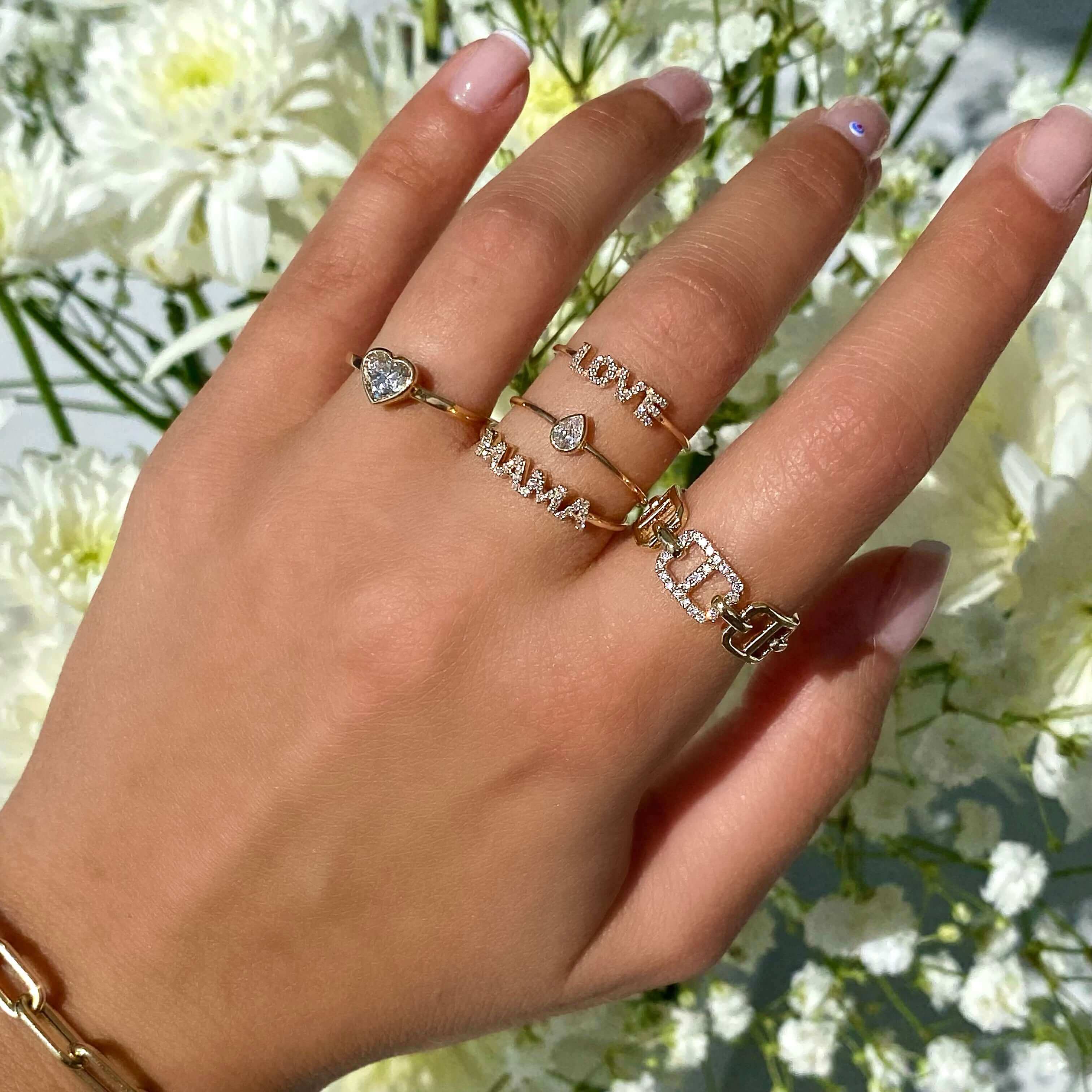 Elegant gold and silver rings with diamonds on a hand amidst white flowers, showcasing our luxury jewelry brand.